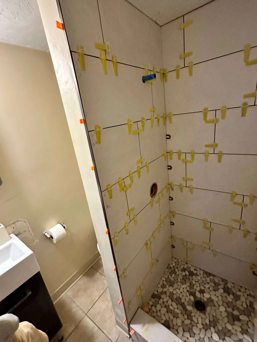 Shower wall tile being set with leveling clips above a pebble floor in Logan, Utah