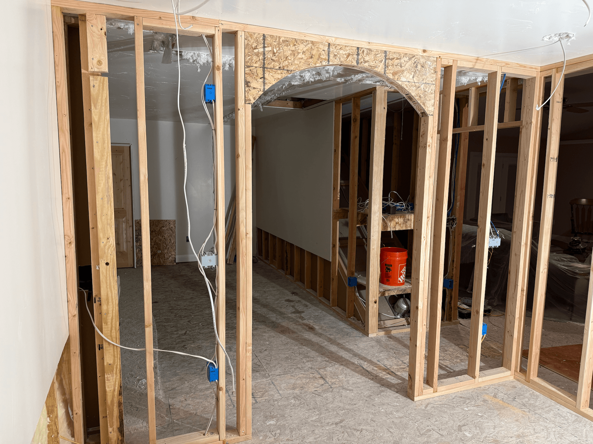 Residential house under construction with scaffolding and wooden framework visible, blue sky background.