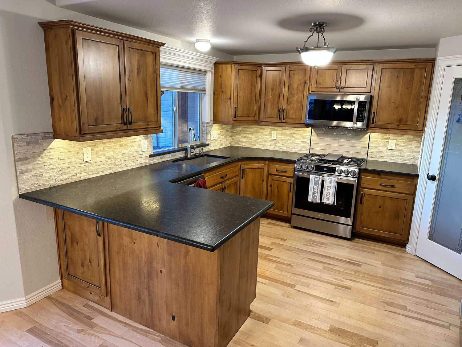 Kitchen remodel with wood cabinets, dark countertops, and a tile backsplash in Cache Valley, Utah