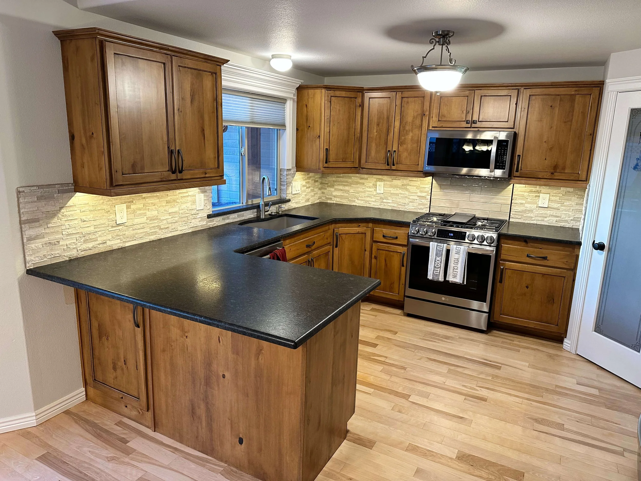 Kitchen remodel in Logan, Utah by ONYX Bros with knotty-alder cabinets, dark counters, and a tile backsplash