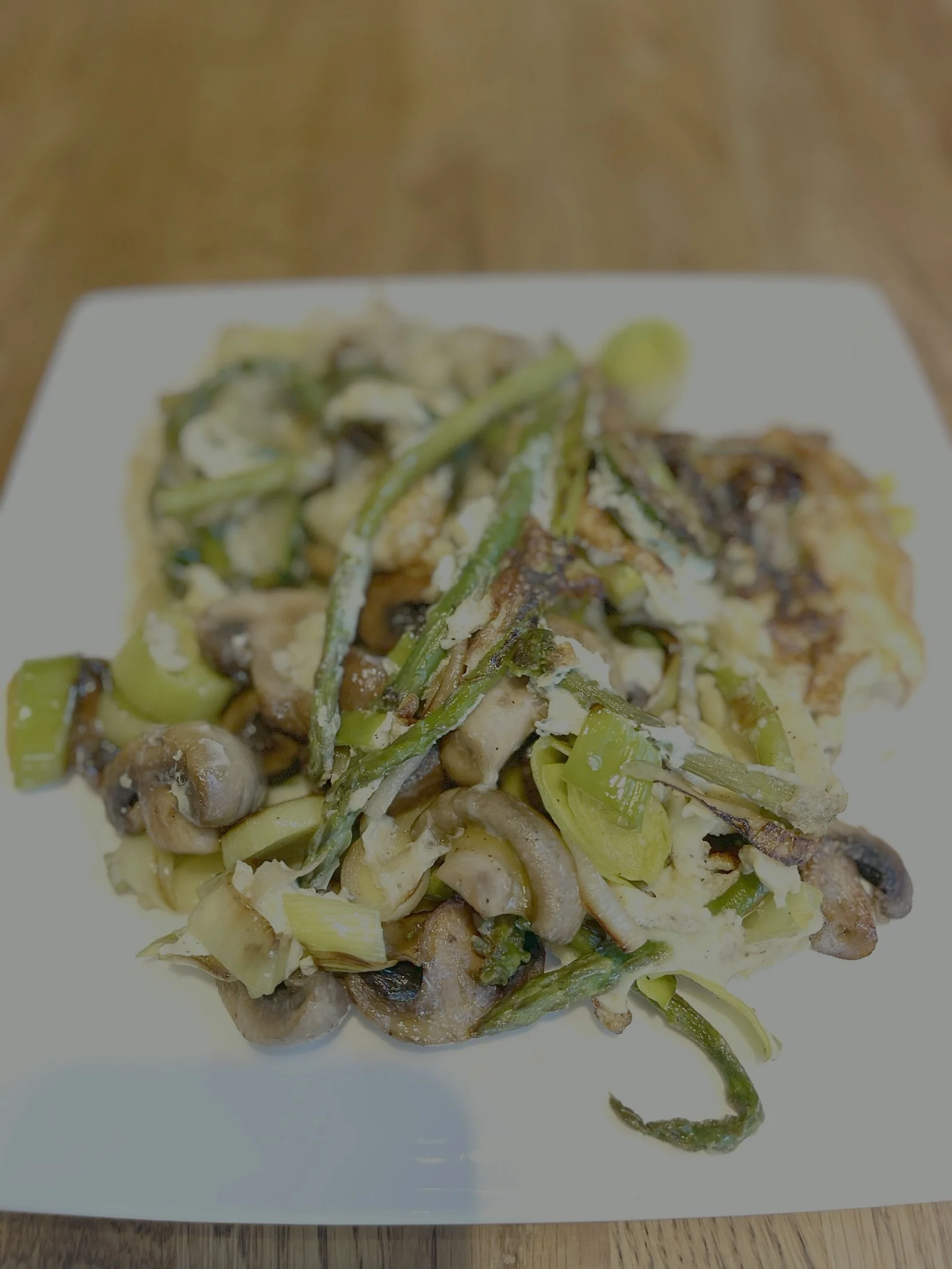 Groentegerecht met champignons, groene uien en asperges op een wit bord.