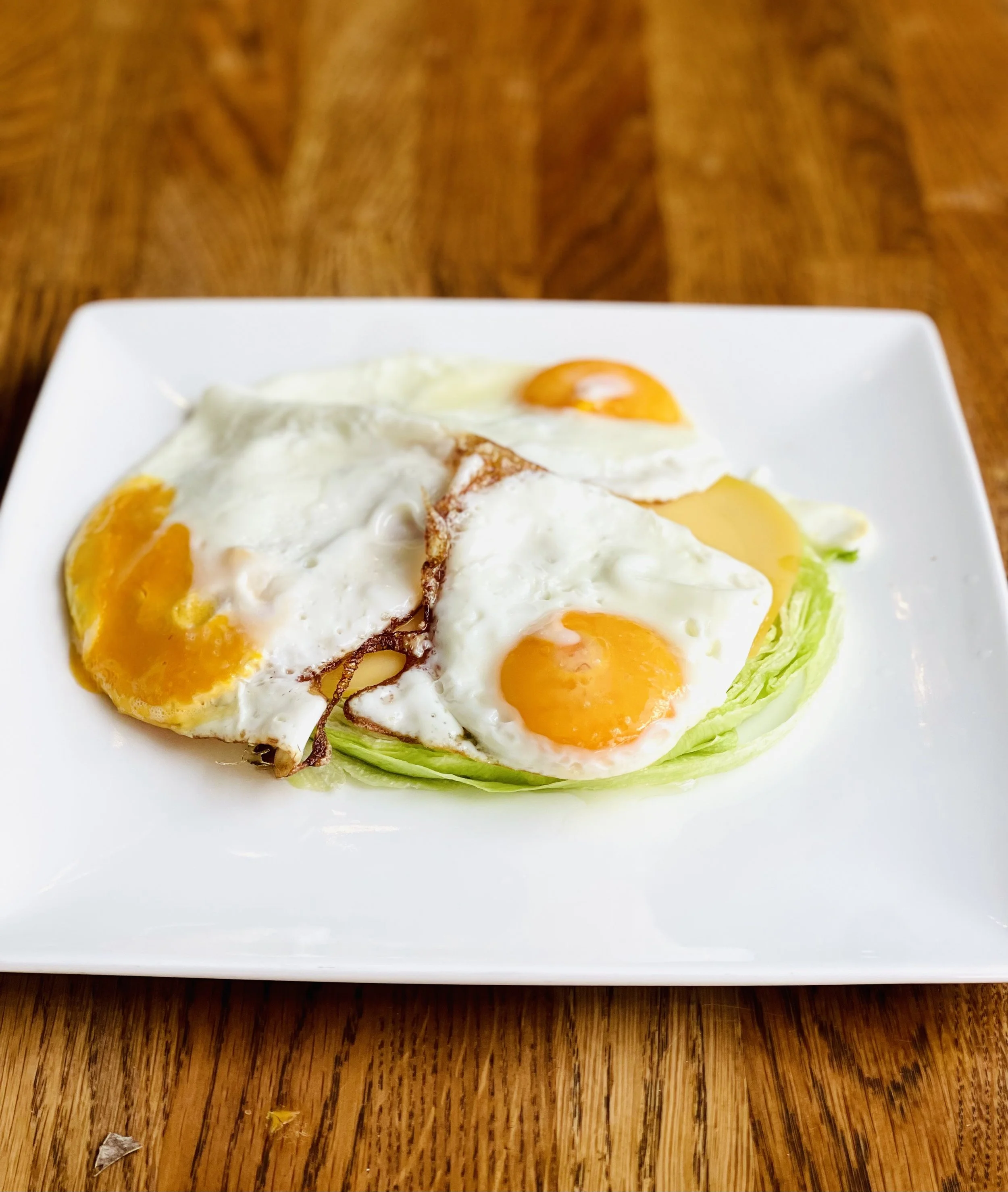 Vier gepocheerde eieren met heldergele dooiers op een bedje van sla op een wit vierkant bord