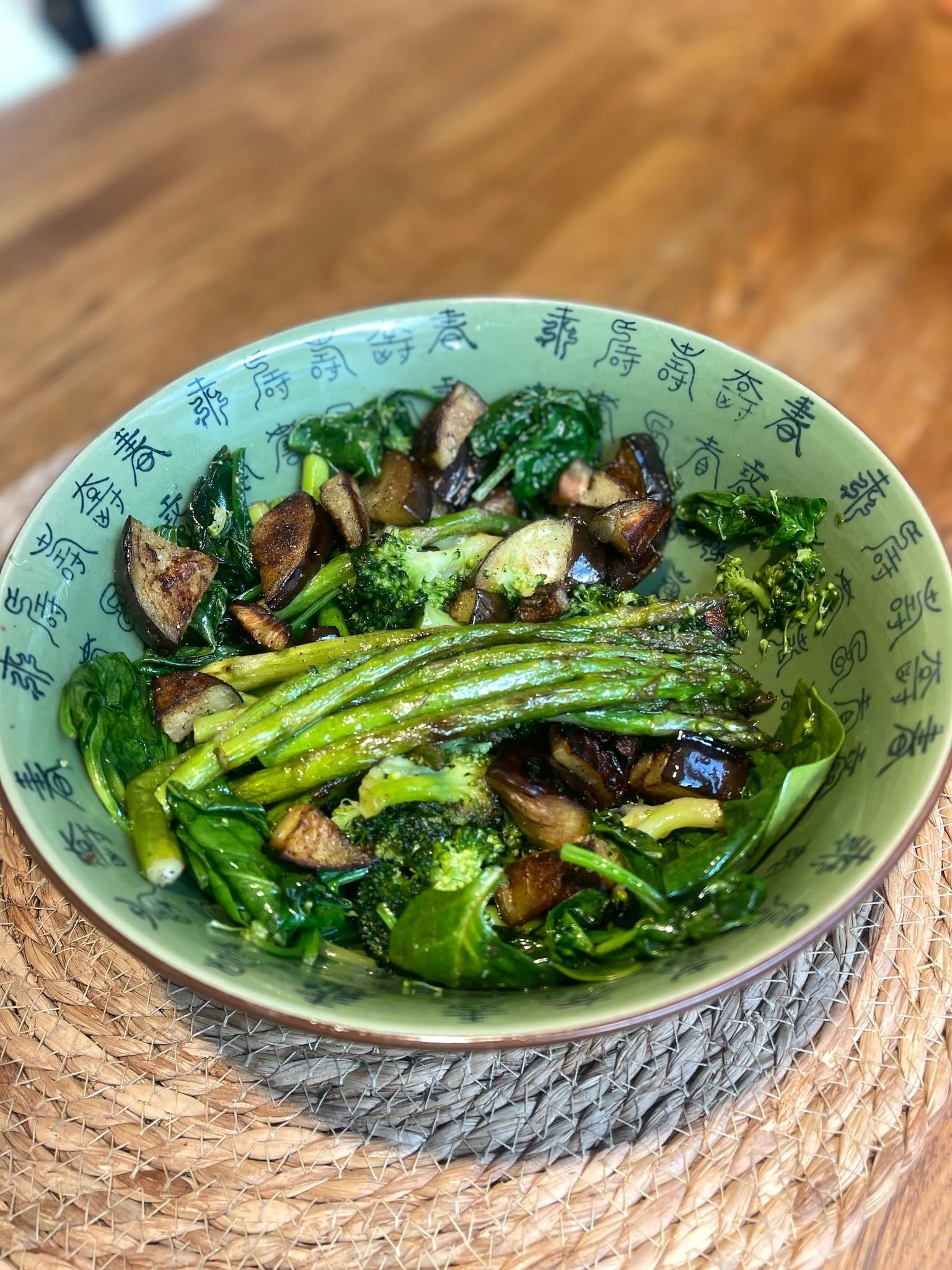 Groene groenten in een kom, inclusief asperges, broccoli, spinazie en aubergine, geserveerd in een groene kom met blauwe Chinese karakters