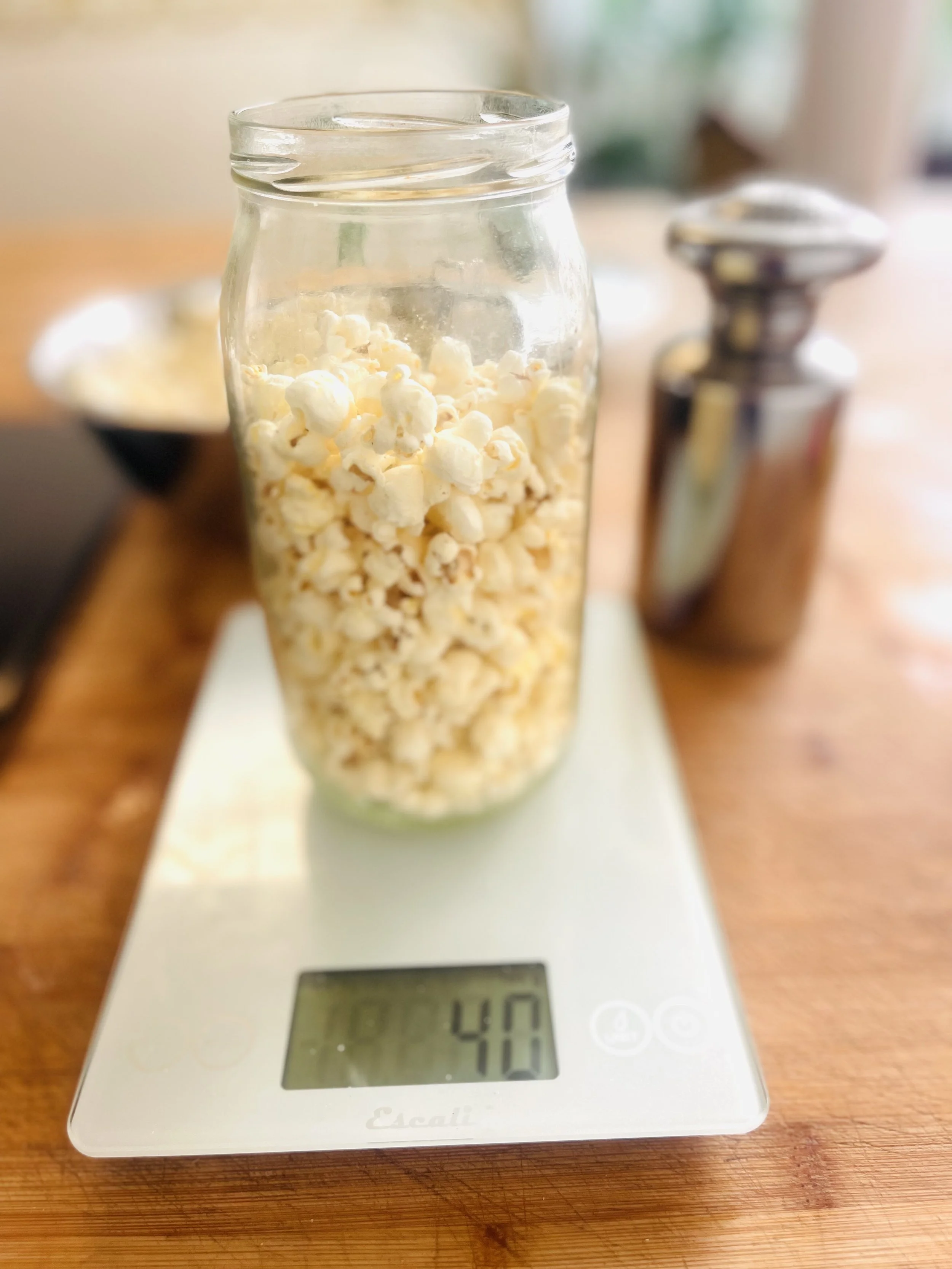 Glaasje met popcorn op een digitale keukenweegschaal die 40 gram aangeeft, op een houten tafel.