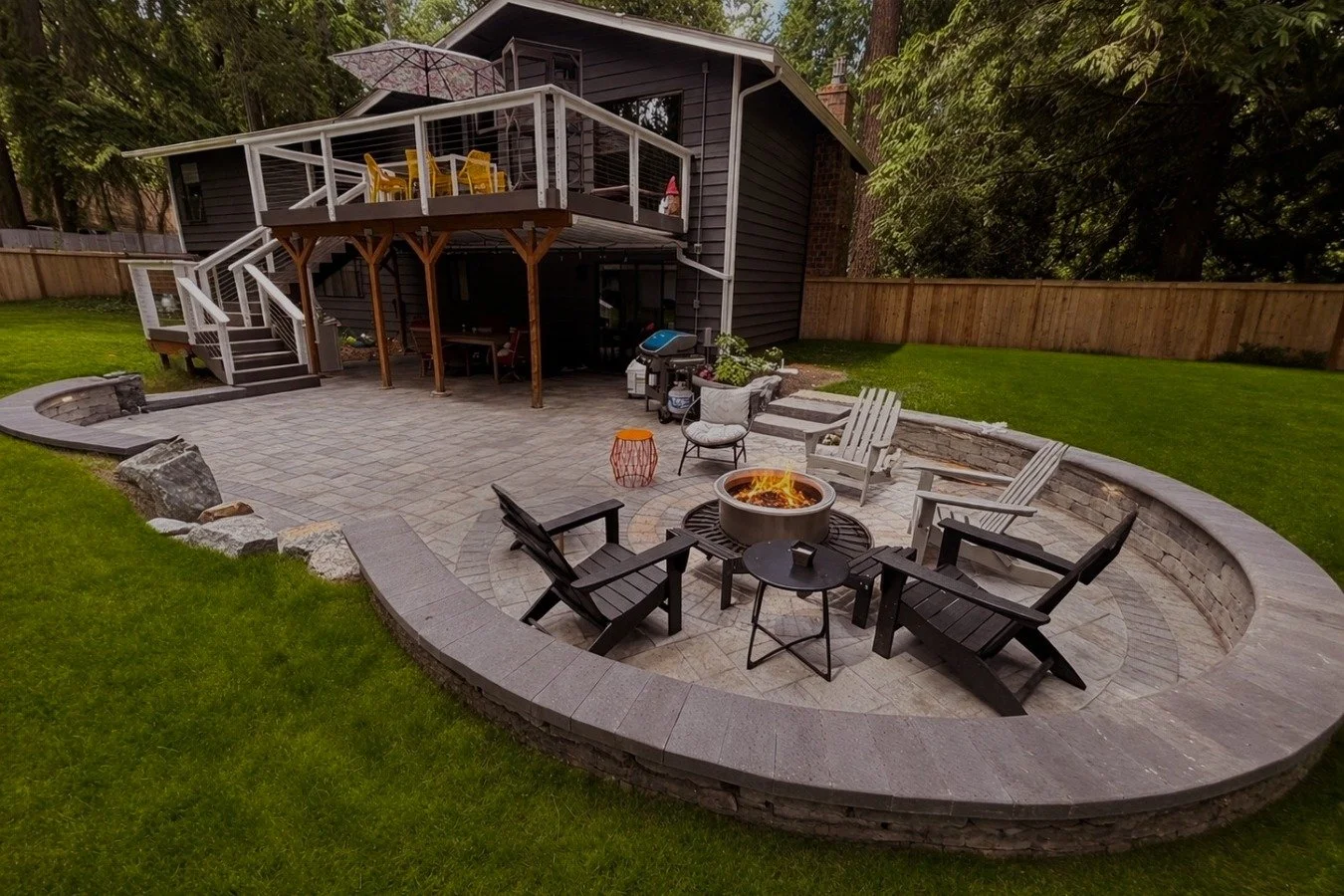 Custom paver patio, patio chairs and a fireplace in a backyard.