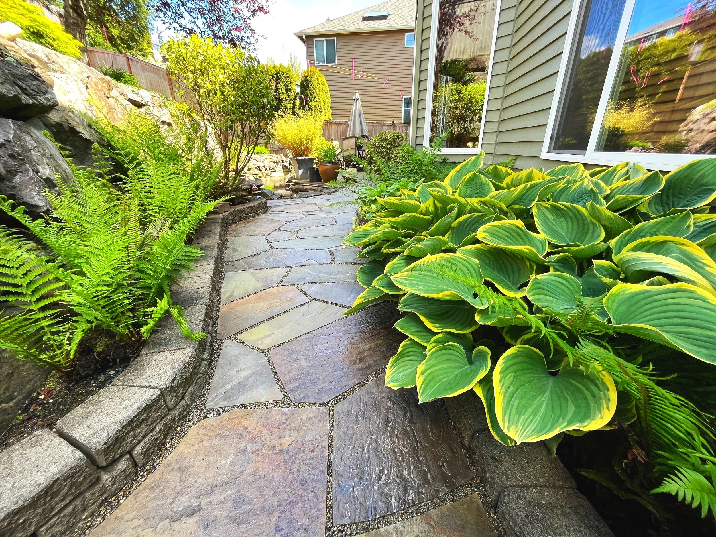 Beautiful custom patio walkaway with retaining walls and lush plants by a Monroe landscaper in Washington.