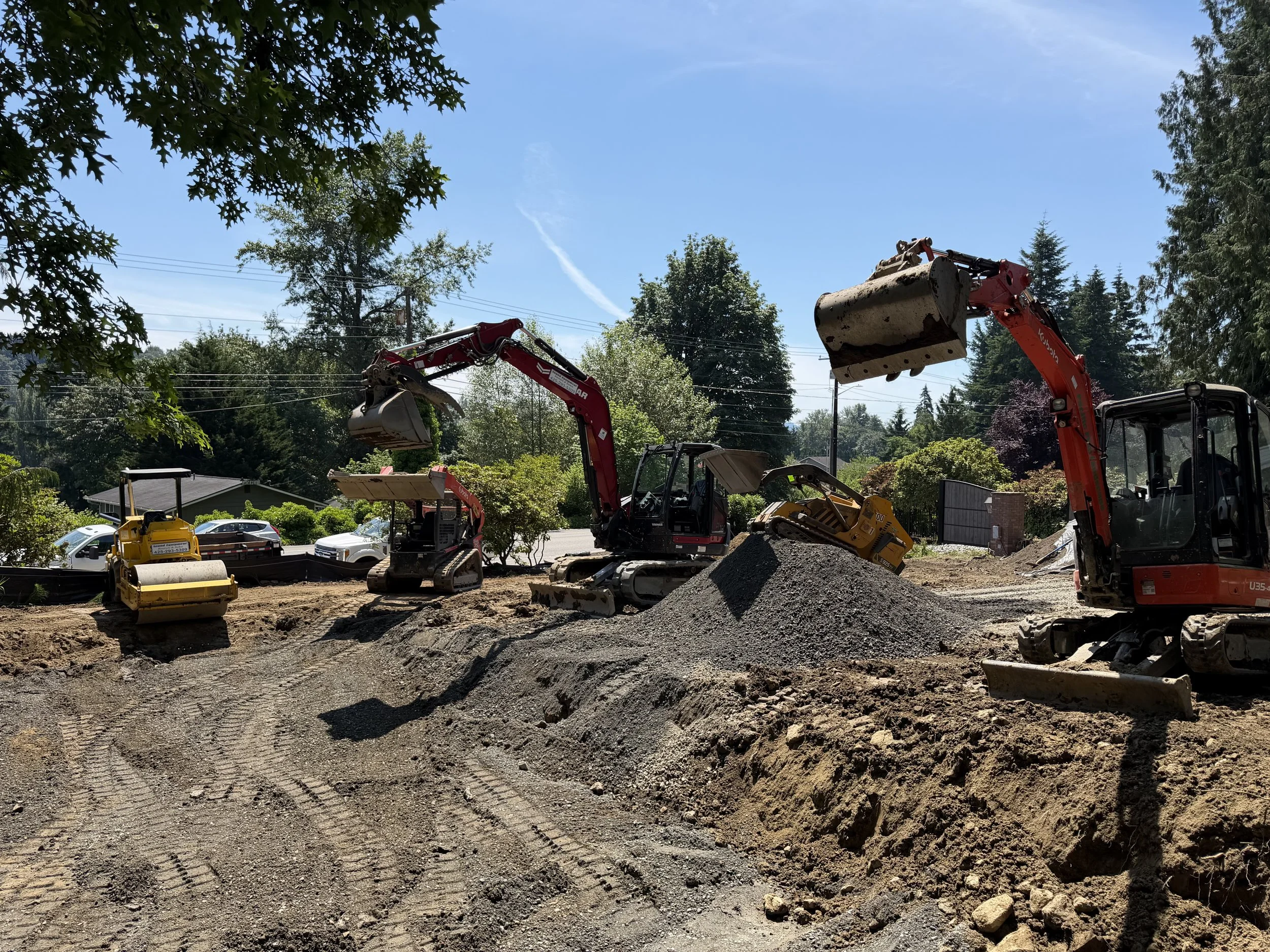 Excavator performing dirt work and trench excavation next to a residential house, by Pacific Pine Landscape in Snohomish County, WA.