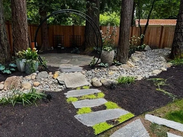 Arched entrance to paver patio with stone steps and dry creek landscape installation.