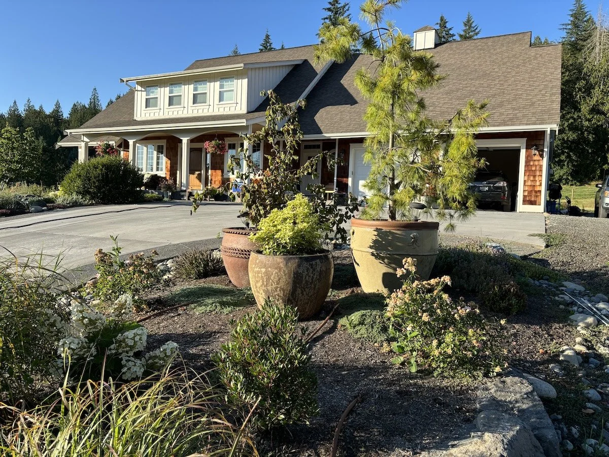 Front yard planting beds and container plants beside a home and driveway.
