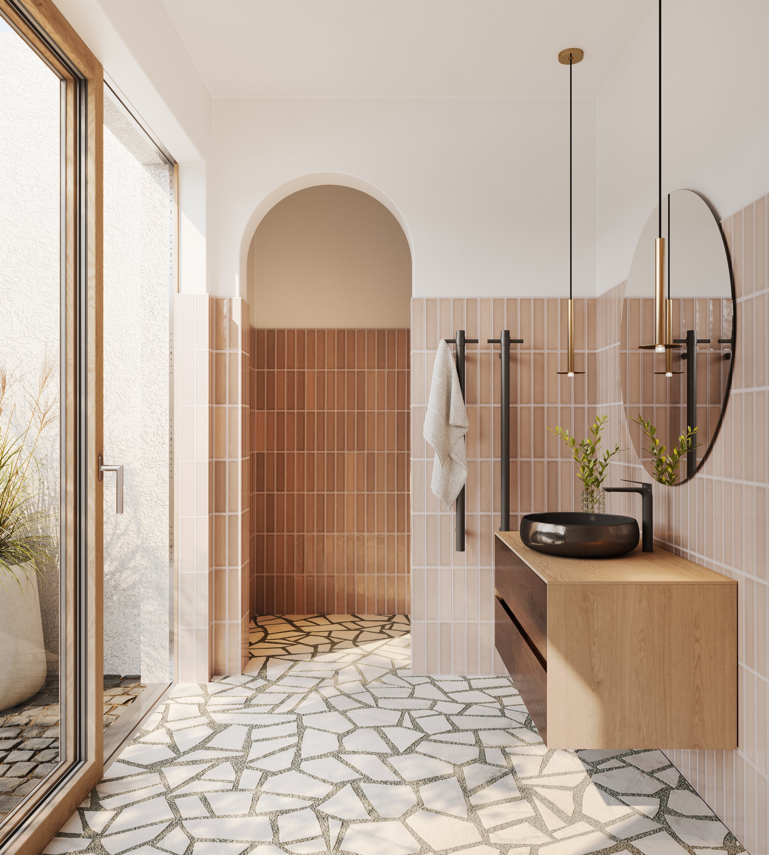 Modern bathroom with pink tiled walls, geometric patterned floor, wooden vanity with black vessel sink, and large round mirror. Pendant lights and plants visible. Room has an archway and a glass door opening to the outside.