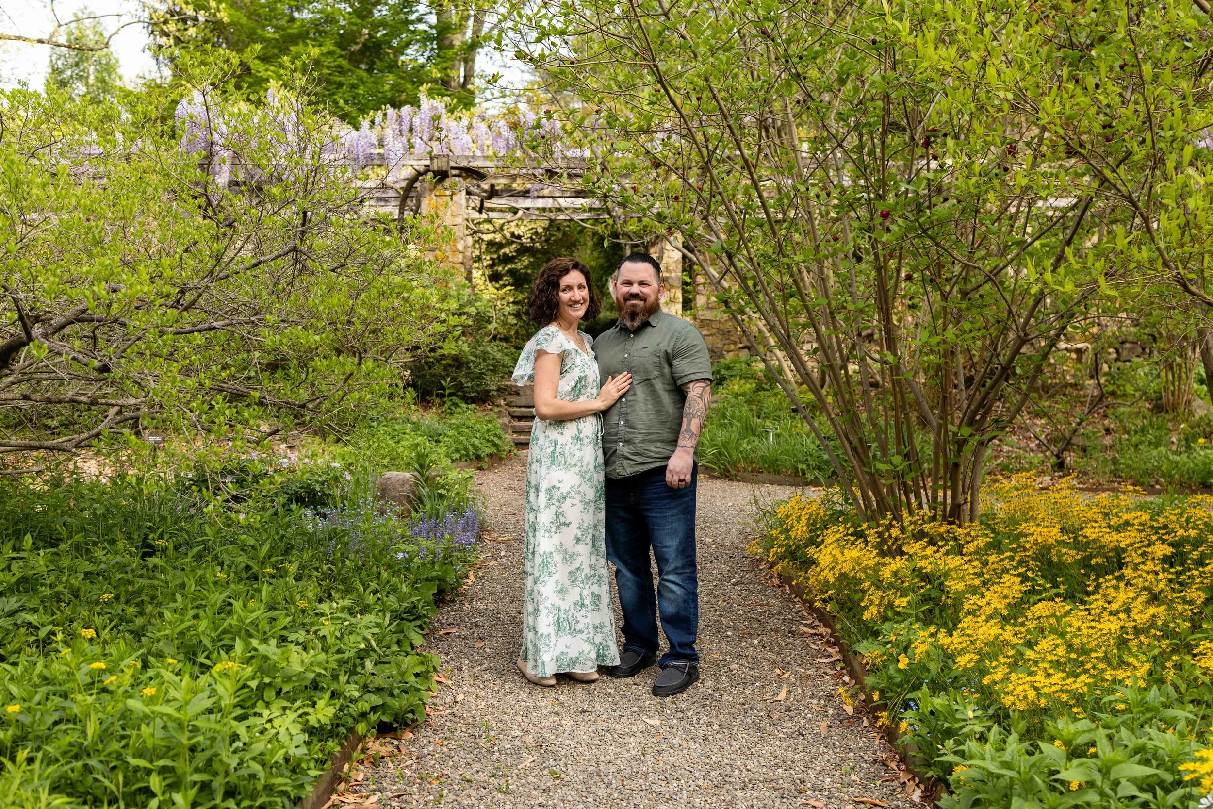 Parents stand in a garden wearing white, blue, and green - family portrait taken by Jennifer Fulton Photography in NJ