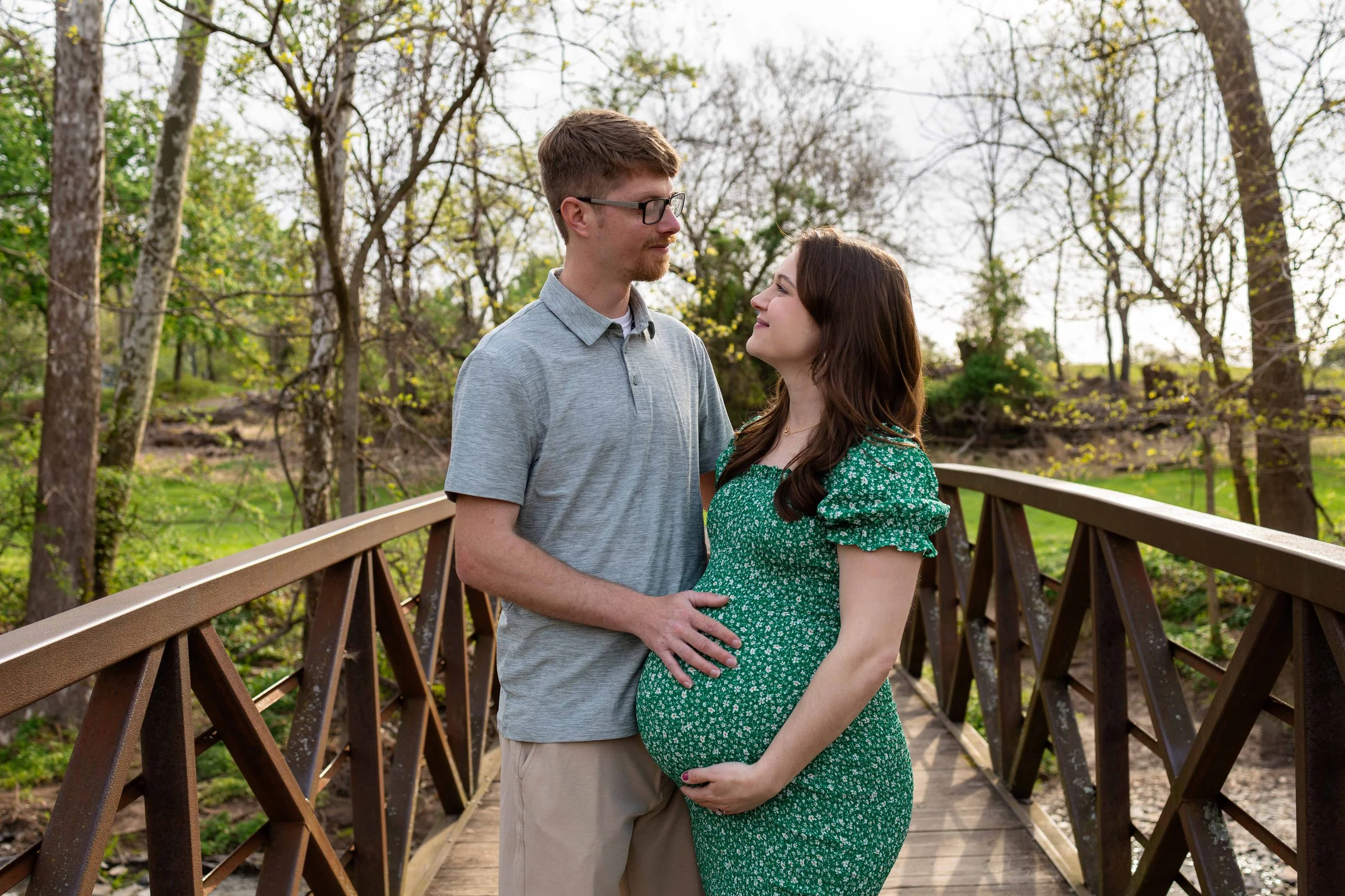 A pregnant couple looks at each other lovingly while standing on a bridge - maternity photo taken by Jennifer Fulton Photography in Hunterdon County, NJ