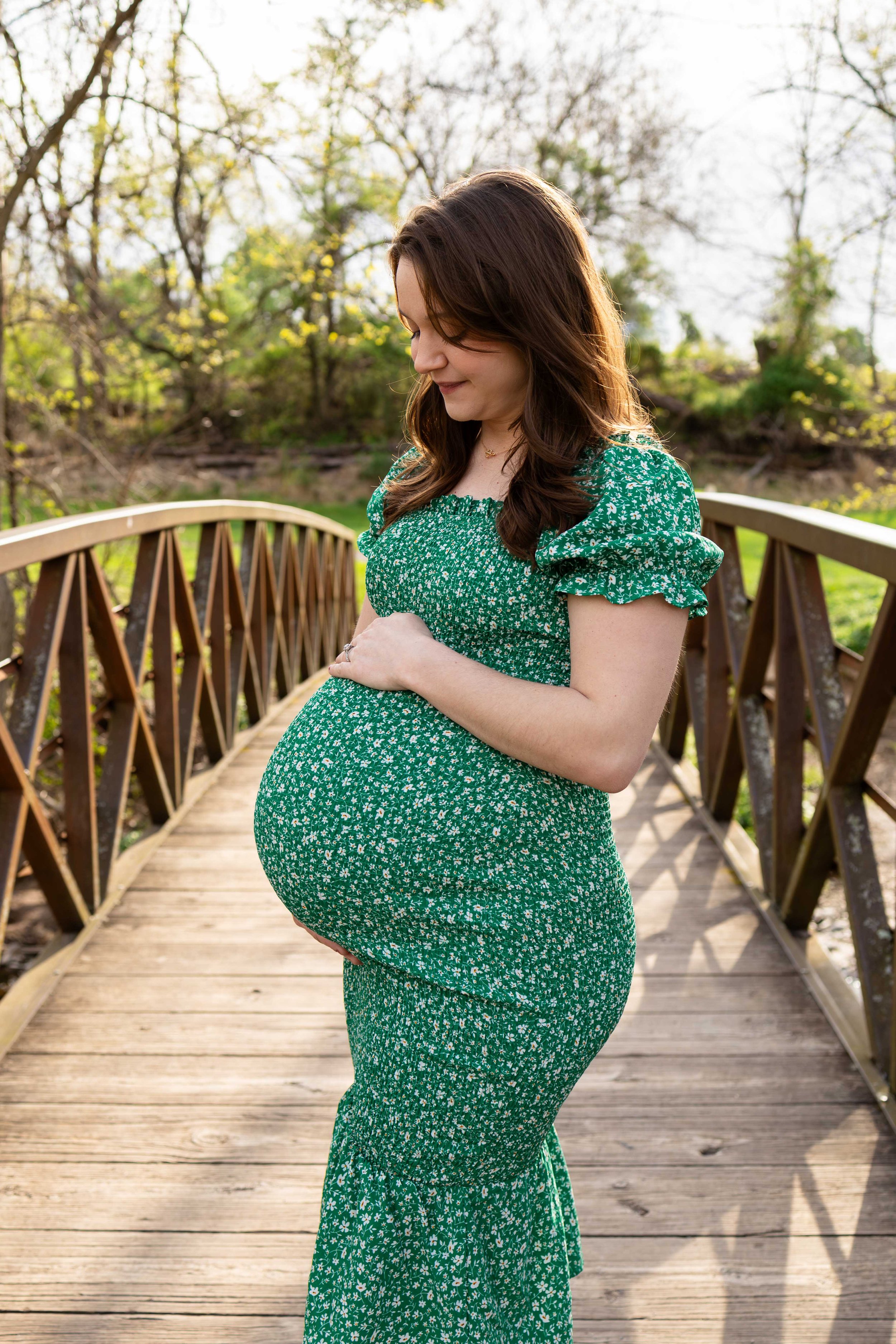 An expecting mother stands on a bridge wearing a green dress - maternity photo taken by Jennifer Fulton Photography in Clinton, NJ