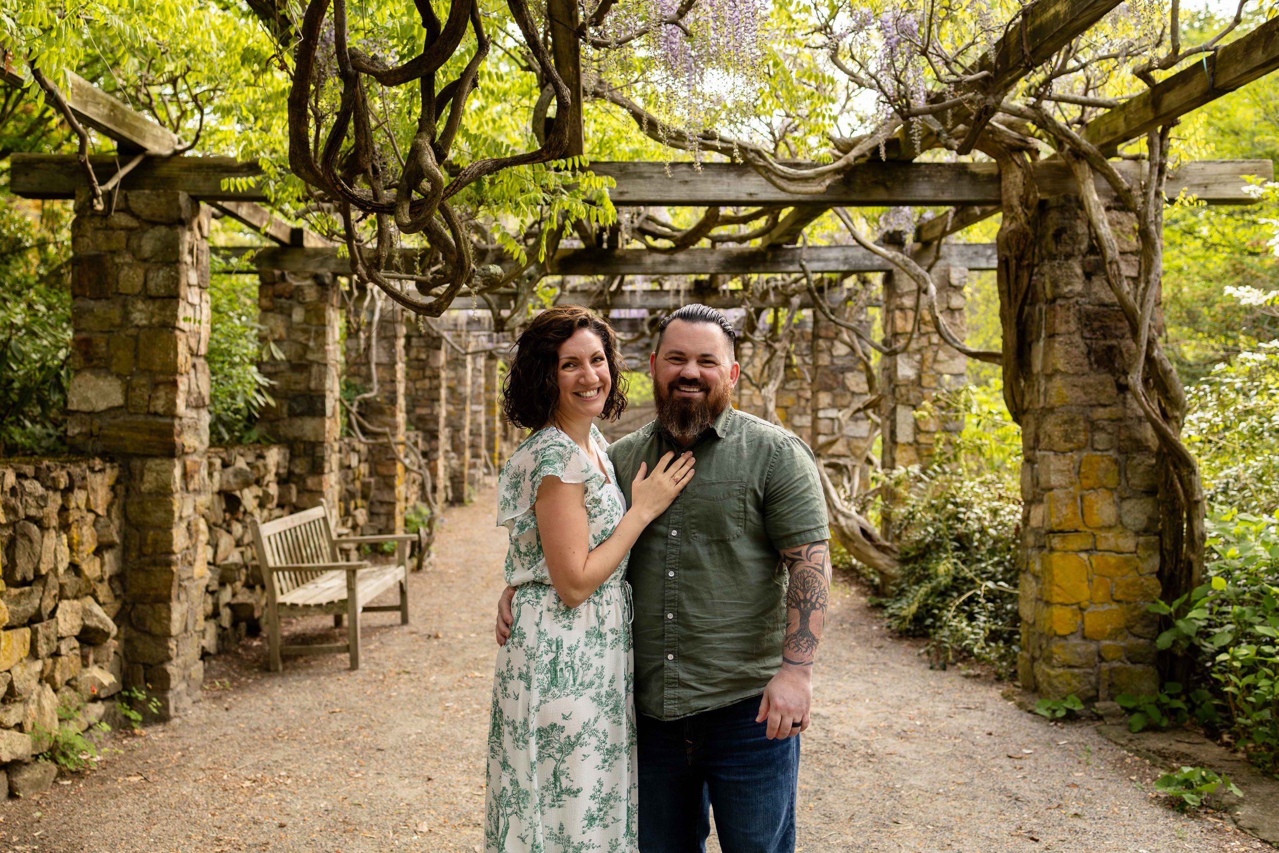 A couple stands under a vine-covered trellis wearing white and green. Couples photo taken by Jennifer Fulton Photography in Somerset County, New Jersey