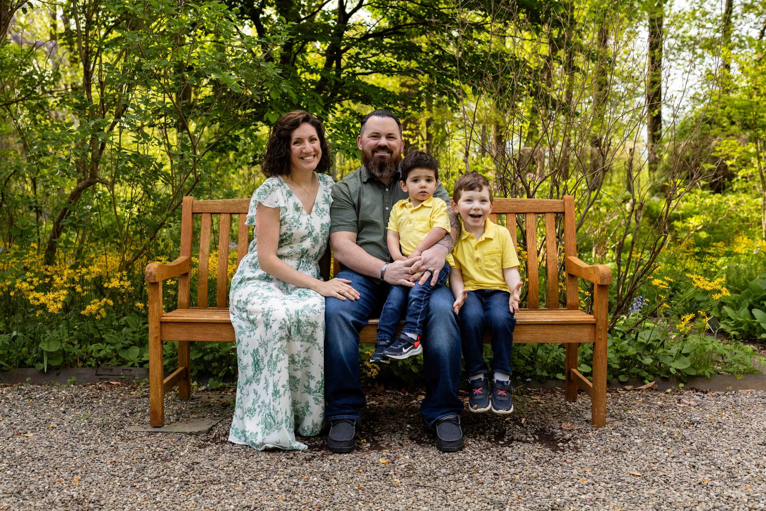 A family of four sits on a bench in a garden - family portrait taken by Jennifer Fulton Photography in Somerset NJ
