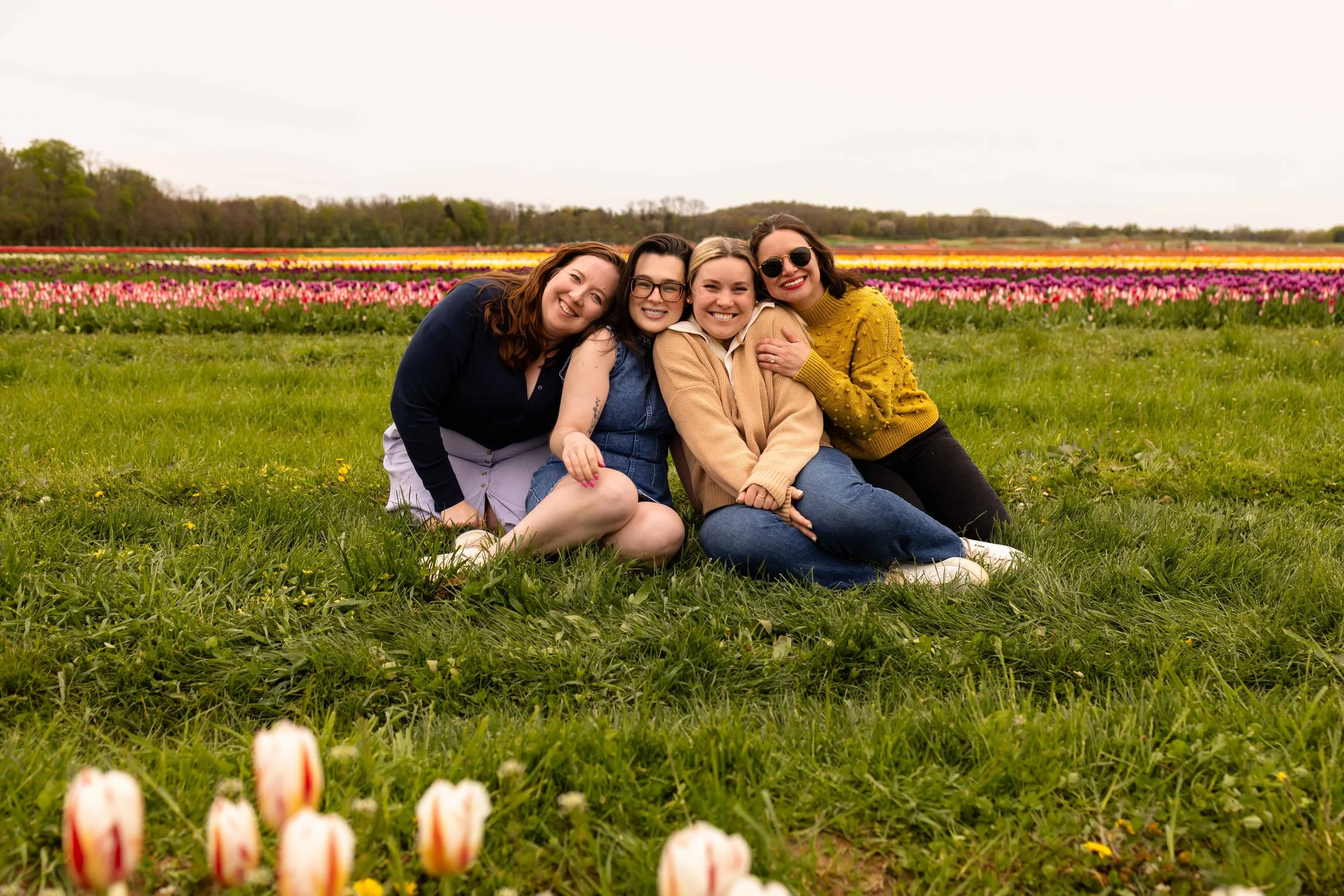 Four friends sit in a flower field in spring - best friends photo taken by Jennifer Fulton Photography in Central New Jersey
