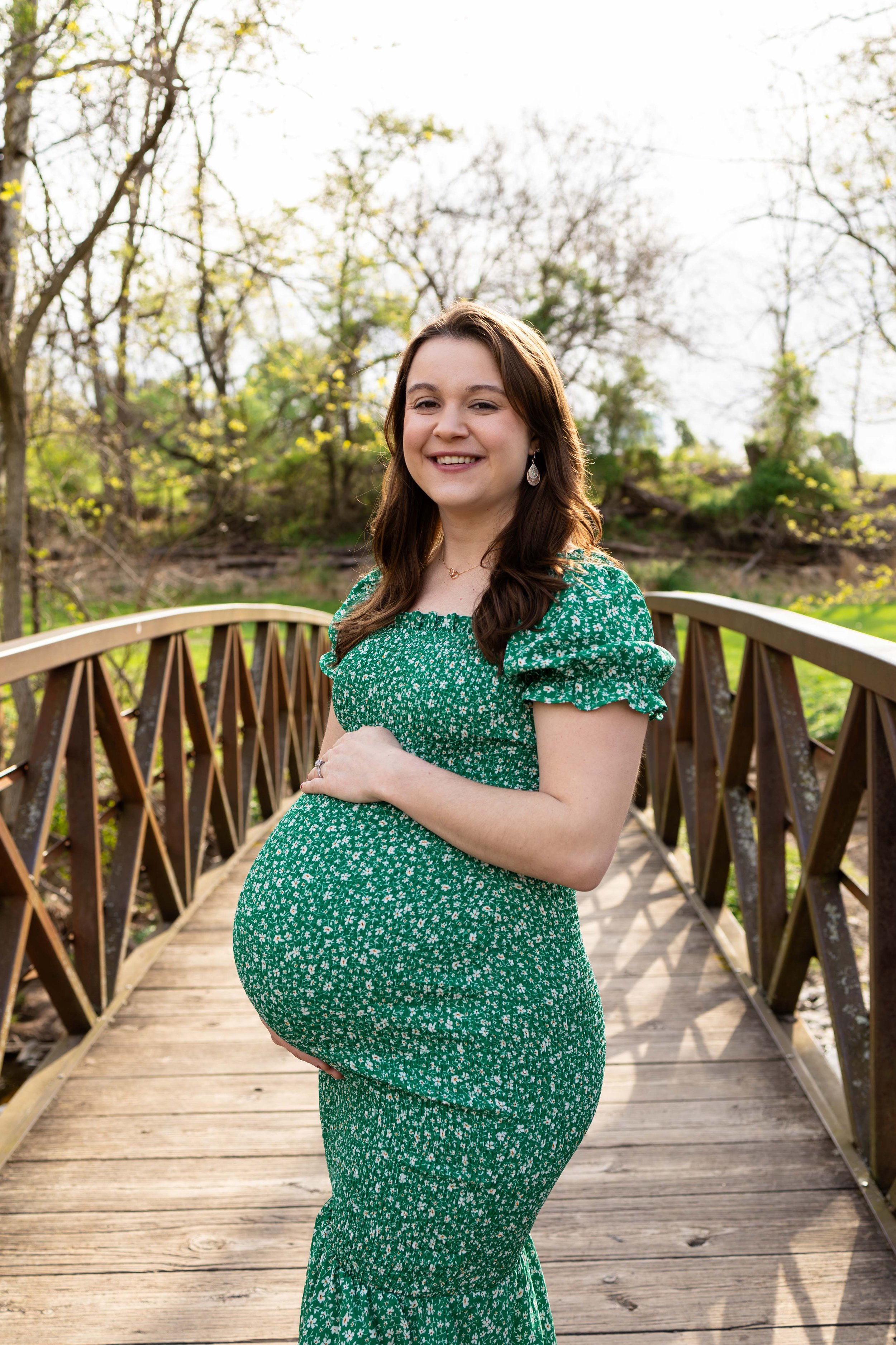 A pregnant mom stands on a bridge wearing a floral dress - maternity portrait taken by Jennifer Fulton Photography in  NJ