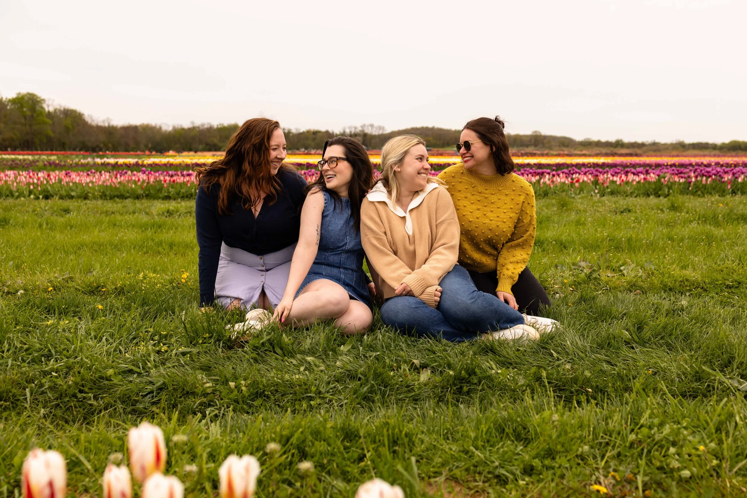 Four friends sit and smile at each other in a tulip field - best friends photo taken by Jennifer Fulton Photography in Central NJ