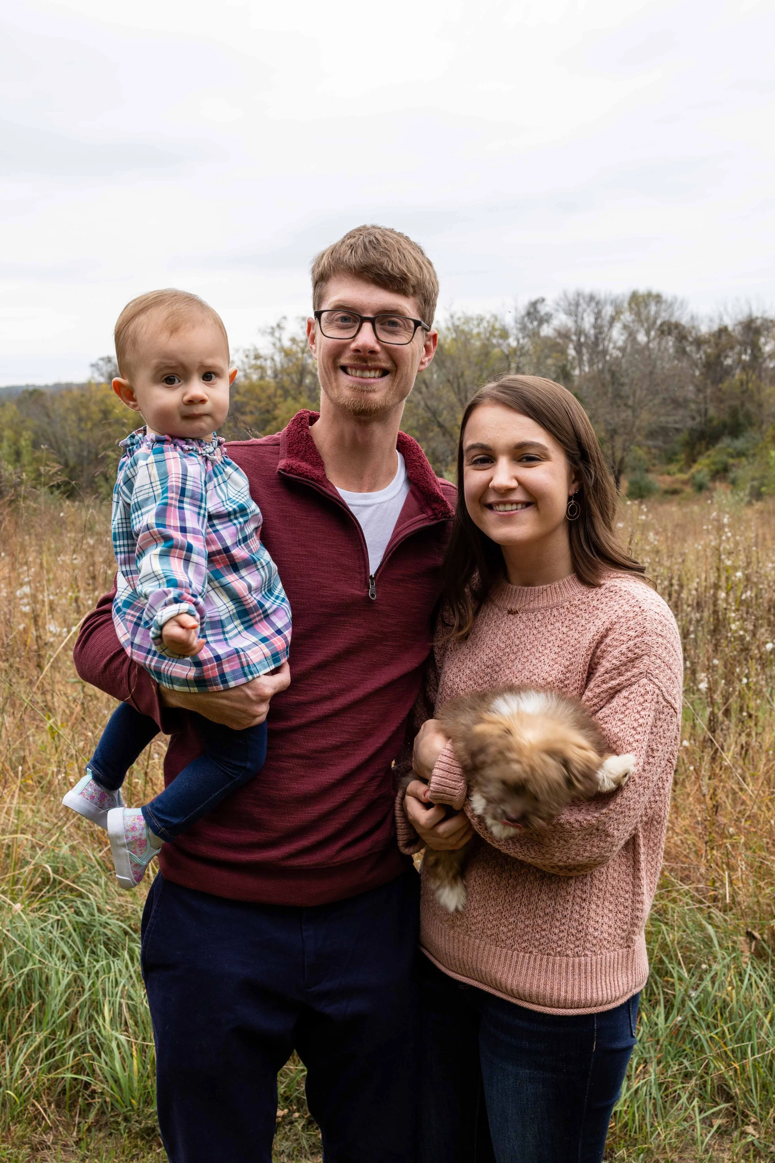 A young family of three wearing pink, burgundy, and blue stand in a field - family photo taken by Jennifer Fulton Photography in Hunterdon County, NJ