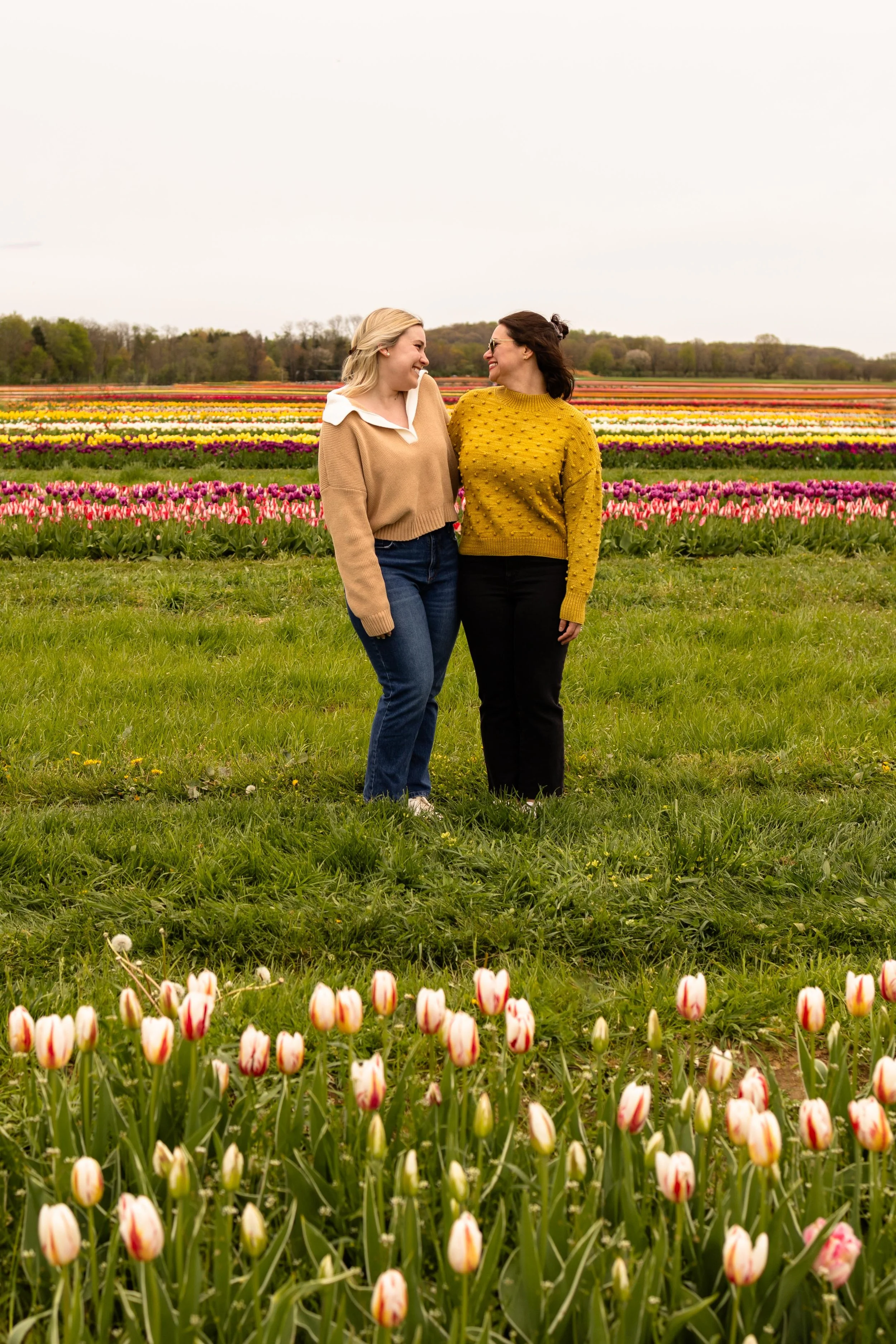 Two friends smile at each other while standing in a tulip field - best friends portrait taken by Jennifer Fulton Photography in NJ