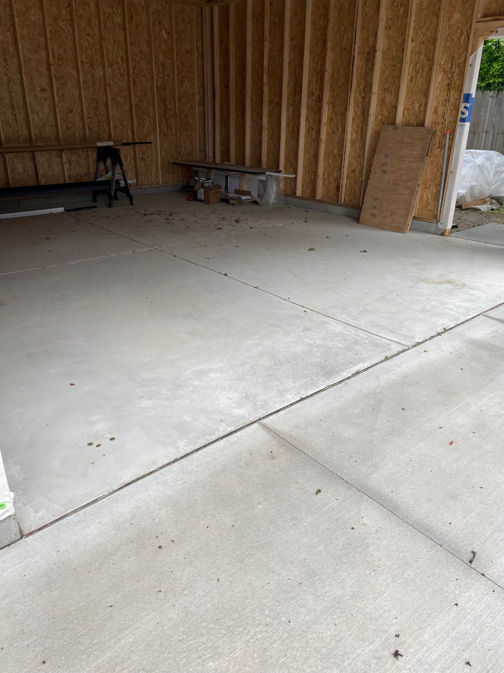 Interior of an unfinished garage with concrete floor, wooden walls, and construction materials scattered.