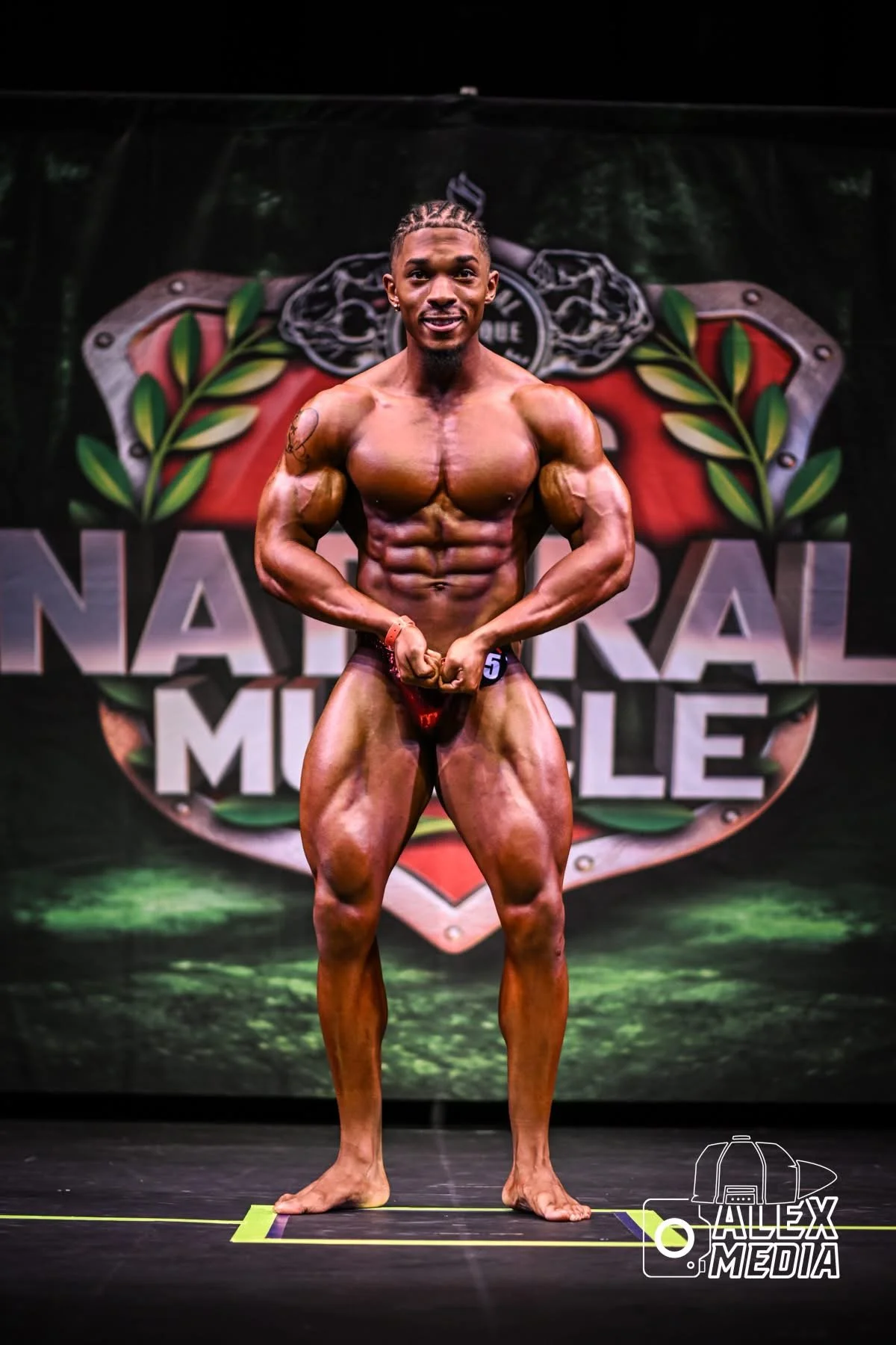 A male bodybuilder on stage in a muscle pose at a natural muscle competition.