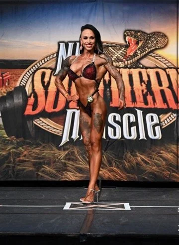 A female bodybuilder posing onstage in a competition, set against a Southern Muscle backdrop.