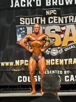 Bodybuilding competition participant posing on stage with a black backdrop displaying "NPC South Central USA".