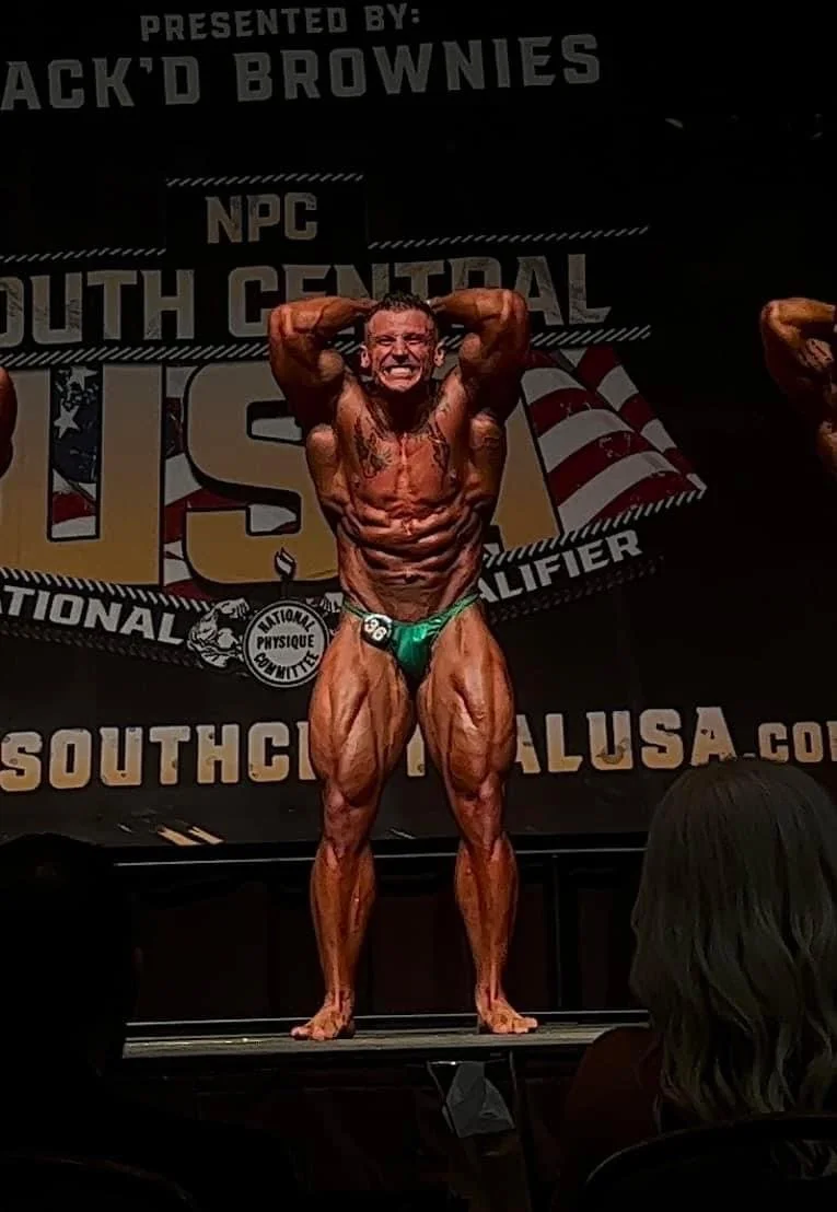 Bodybuilder flexing on stage at USA bodybuilding competition with NPC logo in background, wearing green posing trunks.
