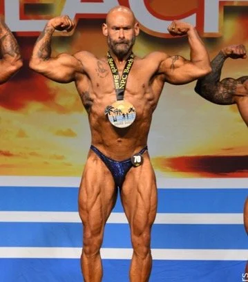 Bodybuilder flexing muscles on stage wearing a medal and a competition number