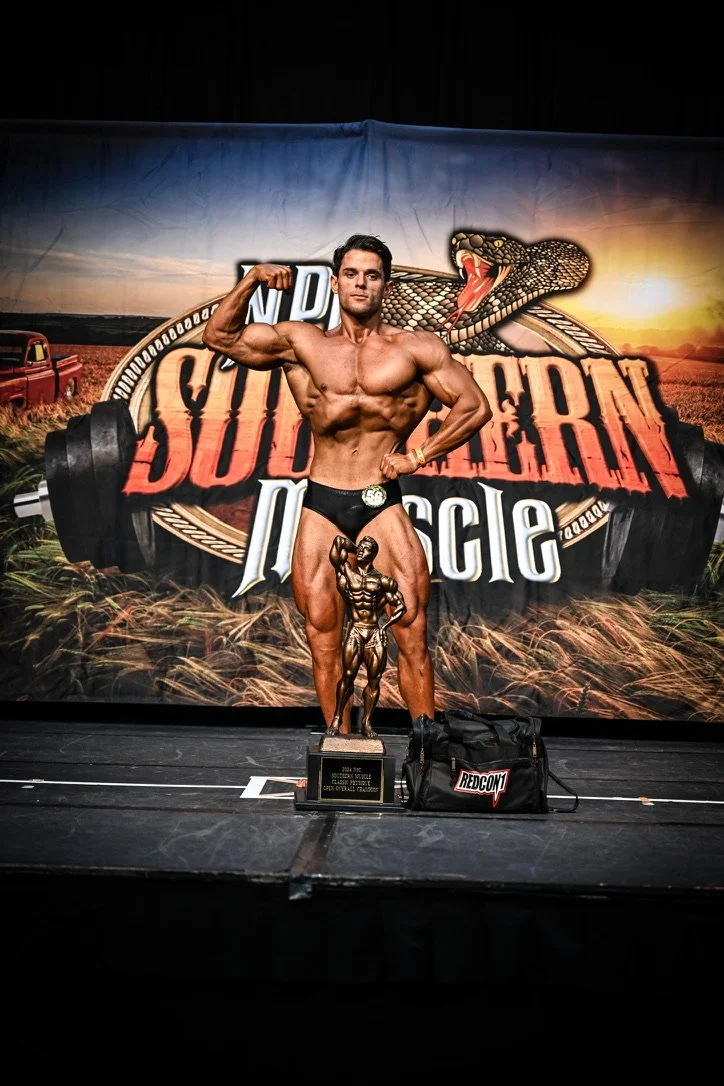 Bodybuilder posing on stage with a trophy at a bodybuilding competition, Southern Muscle event backdrop.