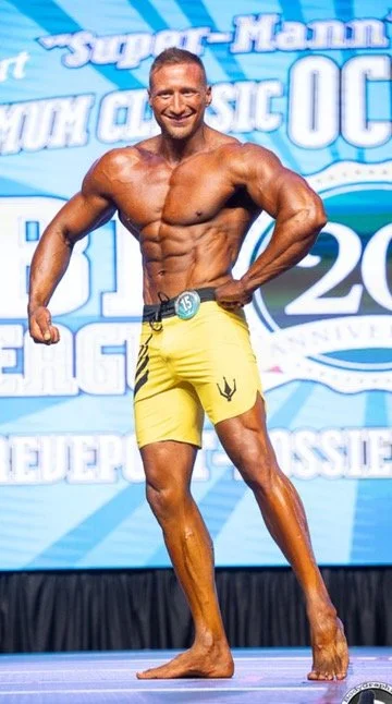 Bodybuilder on stage wearing yellow shorts, striking a pose at a competition.