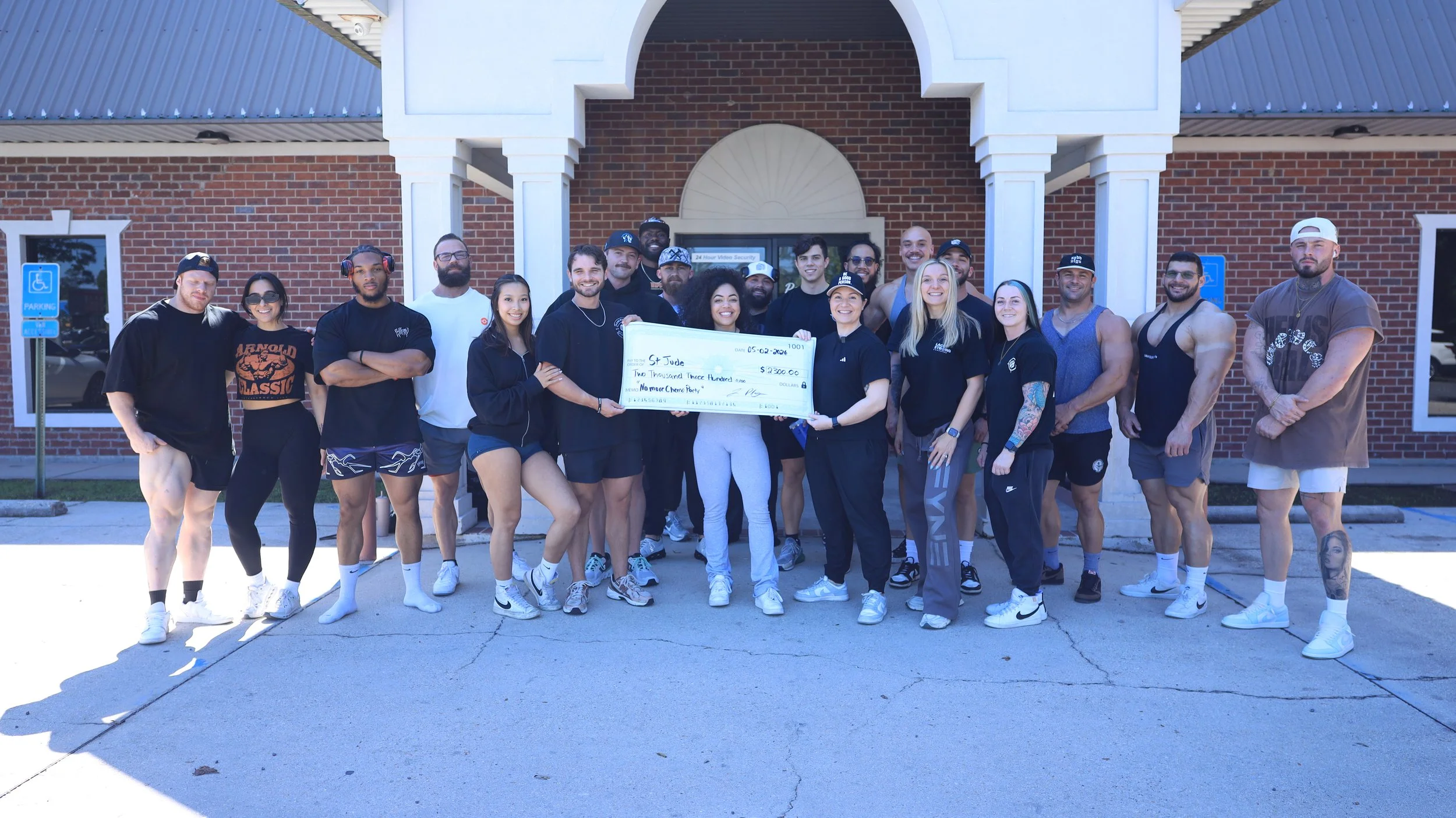 Group of people standing outside a brick building holding a large check for $2,300, smiling and posing for the photo.