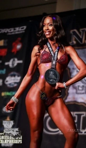 Female bodybuilder posing with a medal at a competition, wearing a bikini on stage.