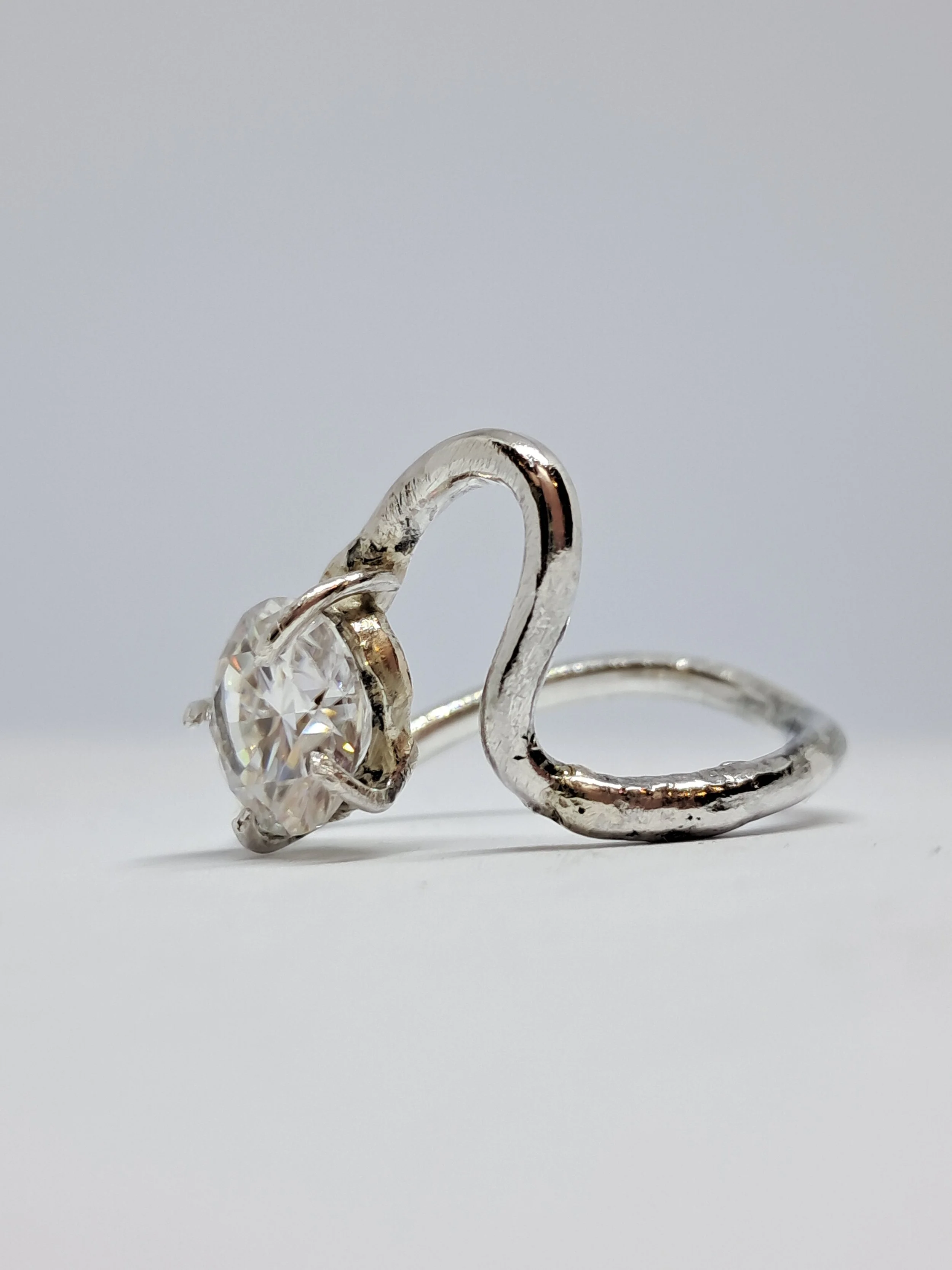 Close-up of a silver ring with a large, clear gemstone resembling a diamond, set in a prong setting, against a plain white background.