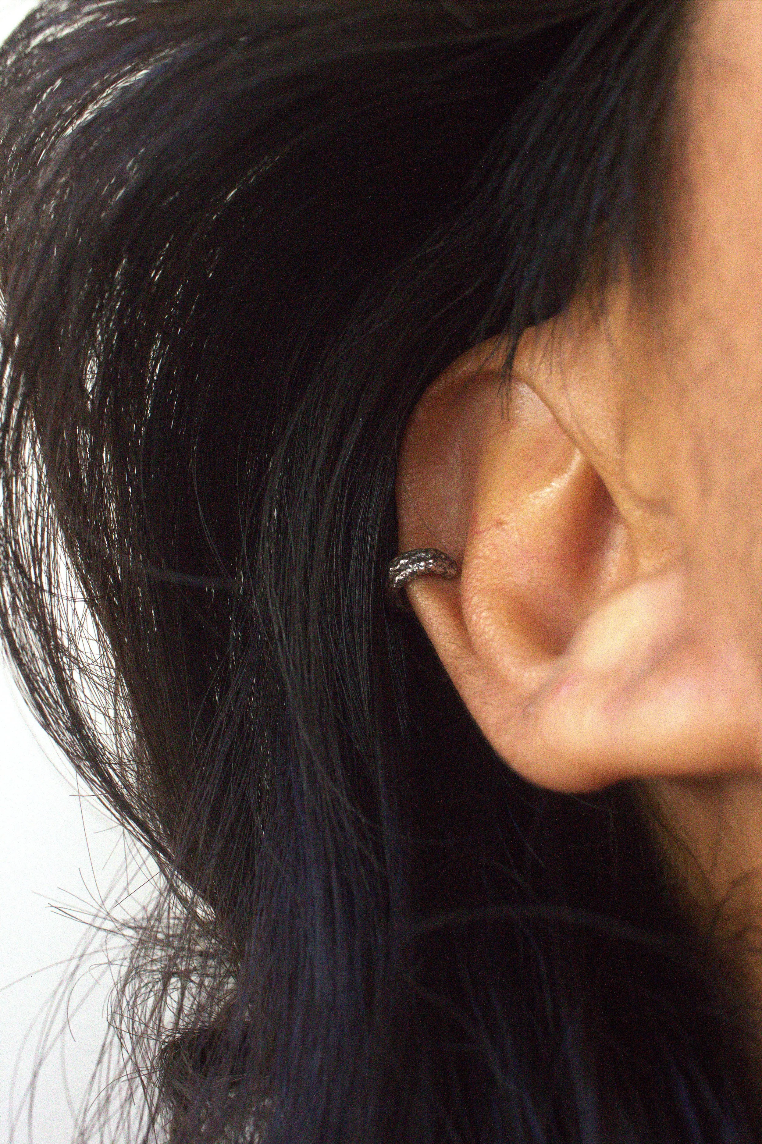Close-up of a person's ear with black hair and a small hoop earring.