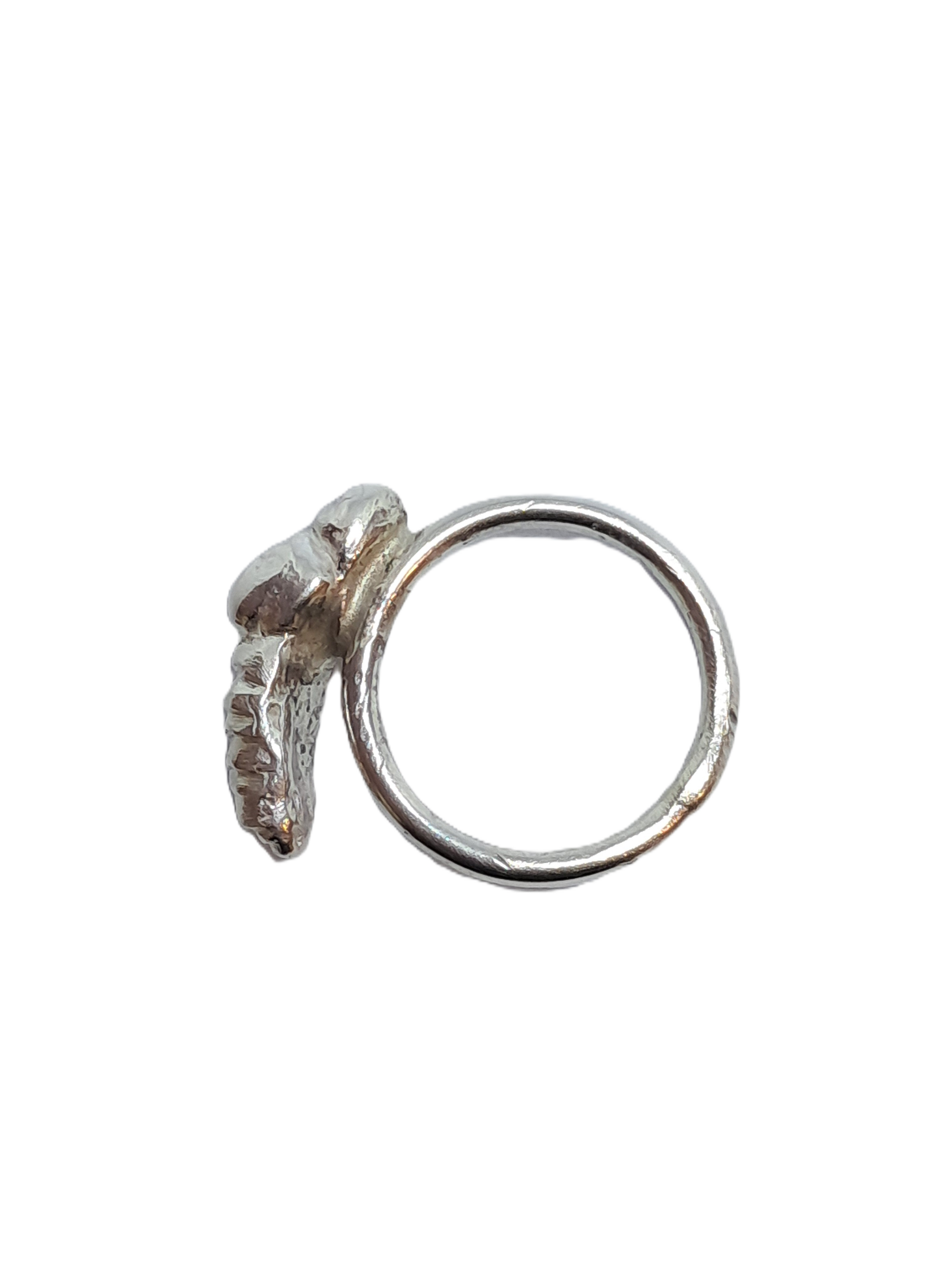 Close-up of a silver ring with textured and smooth surfaces, featuring an irregular shaped design on top.