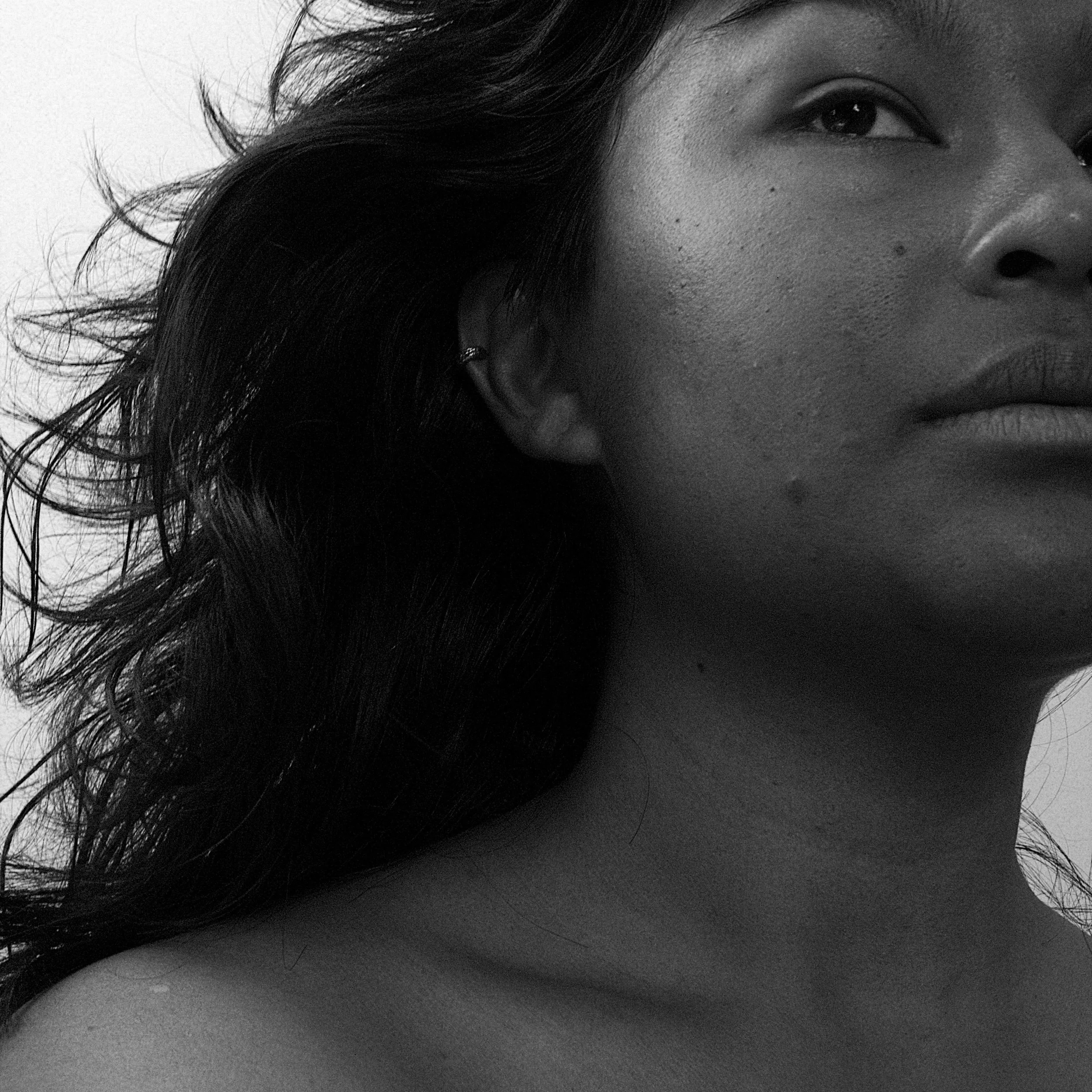 Close-up black and white portrait of a Jade Hardy with wavy hair, showing part of her face and shoulder with a ear cuff on her side ear.