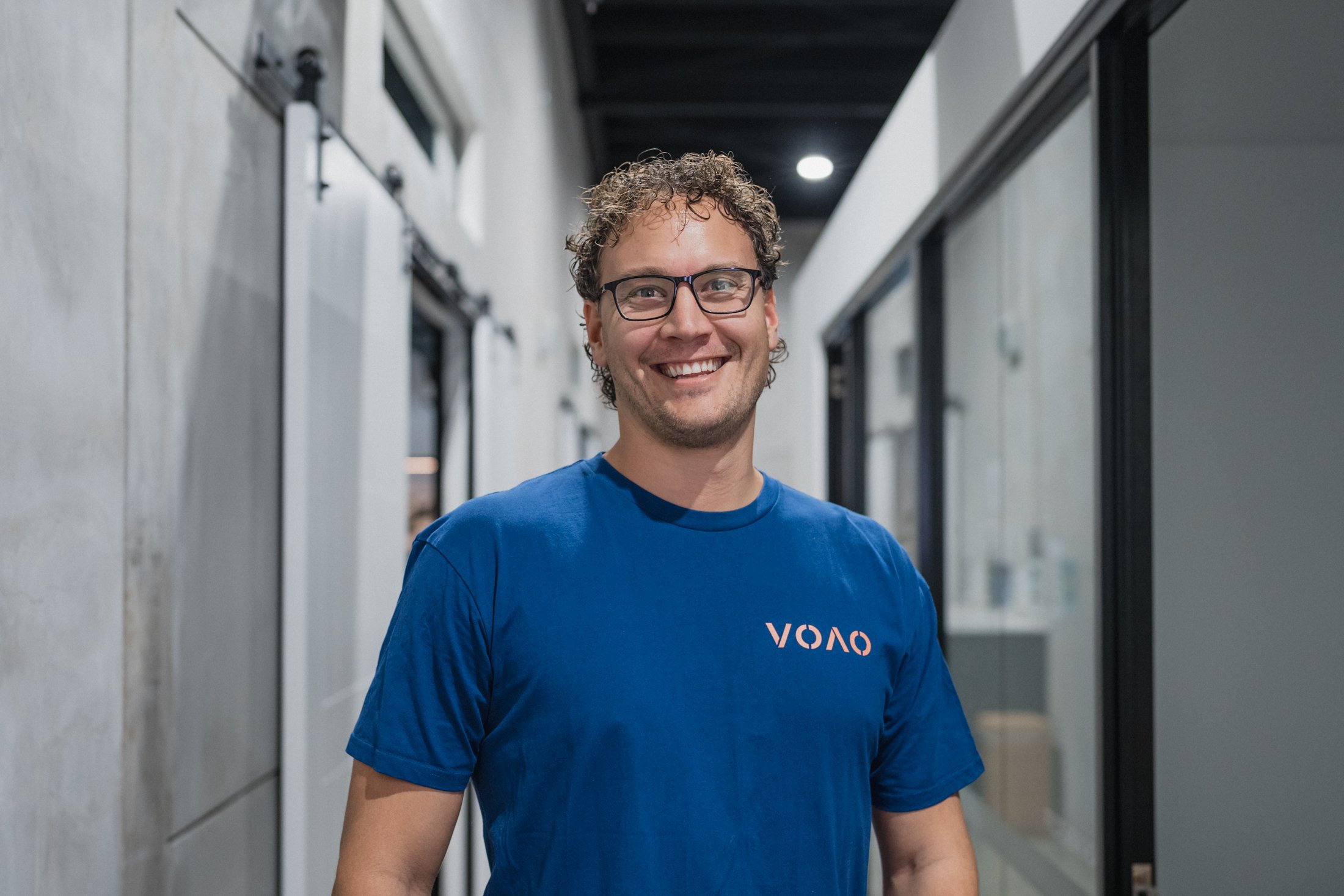 Man smiling, wearing glasses and a light-colored shirt, arms crossed.