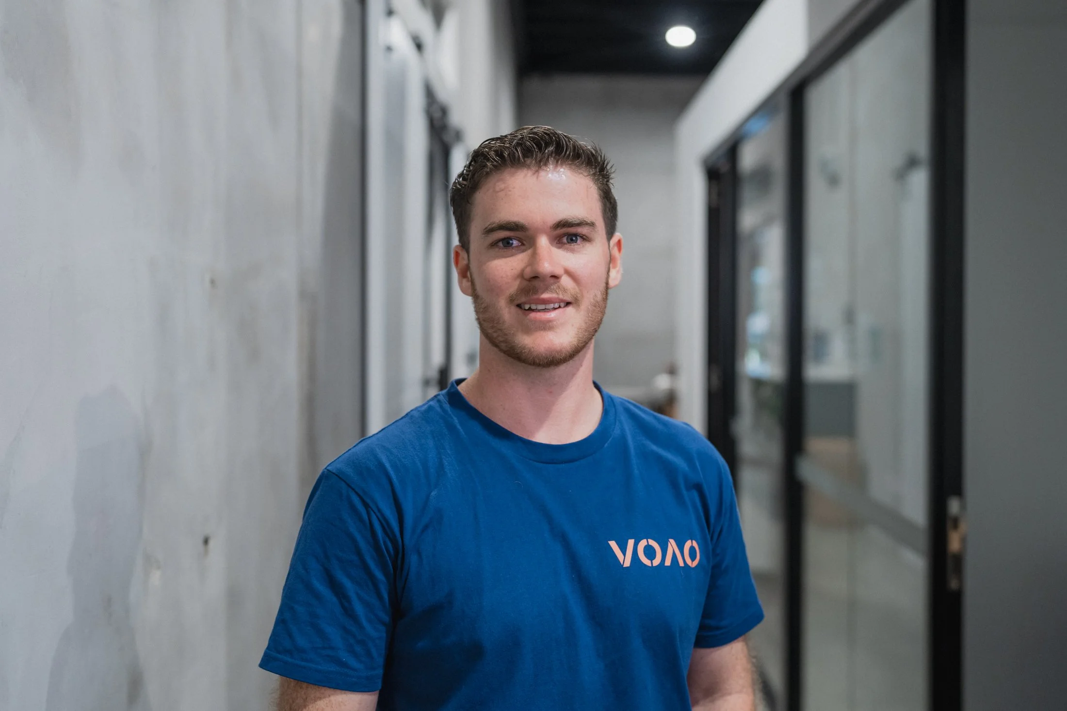Man in a light blue shirt smiling against a plain background.