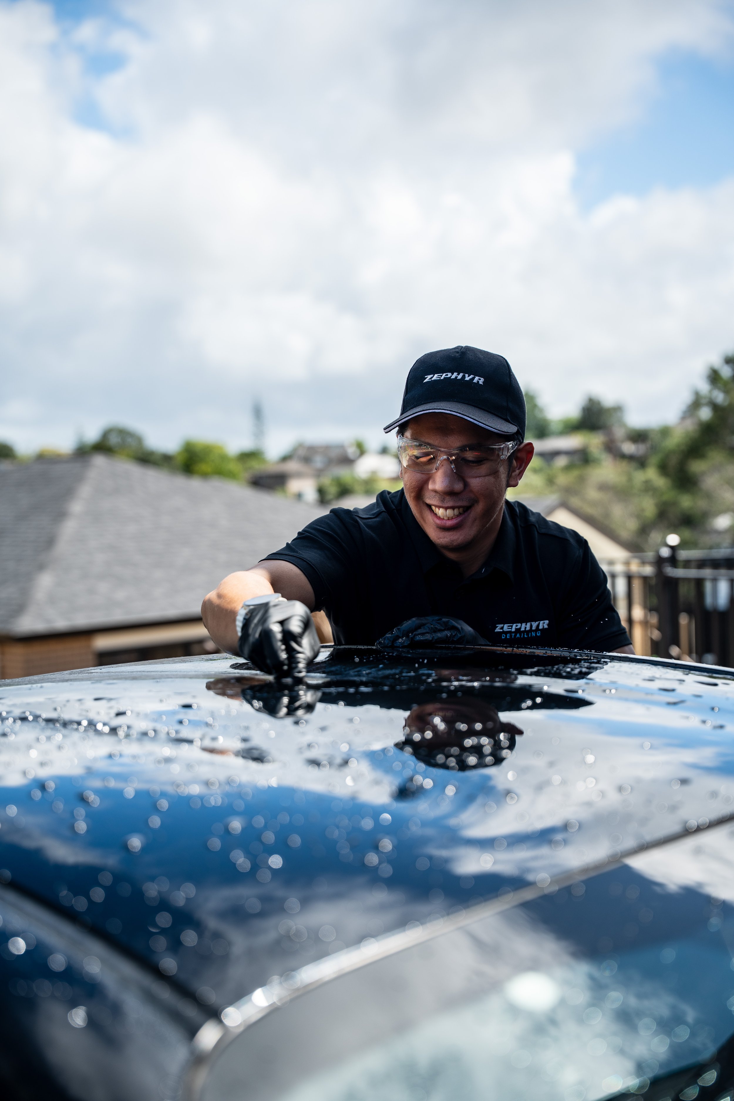 Man polishing the roof of a black car outdoors under cloudy sky.