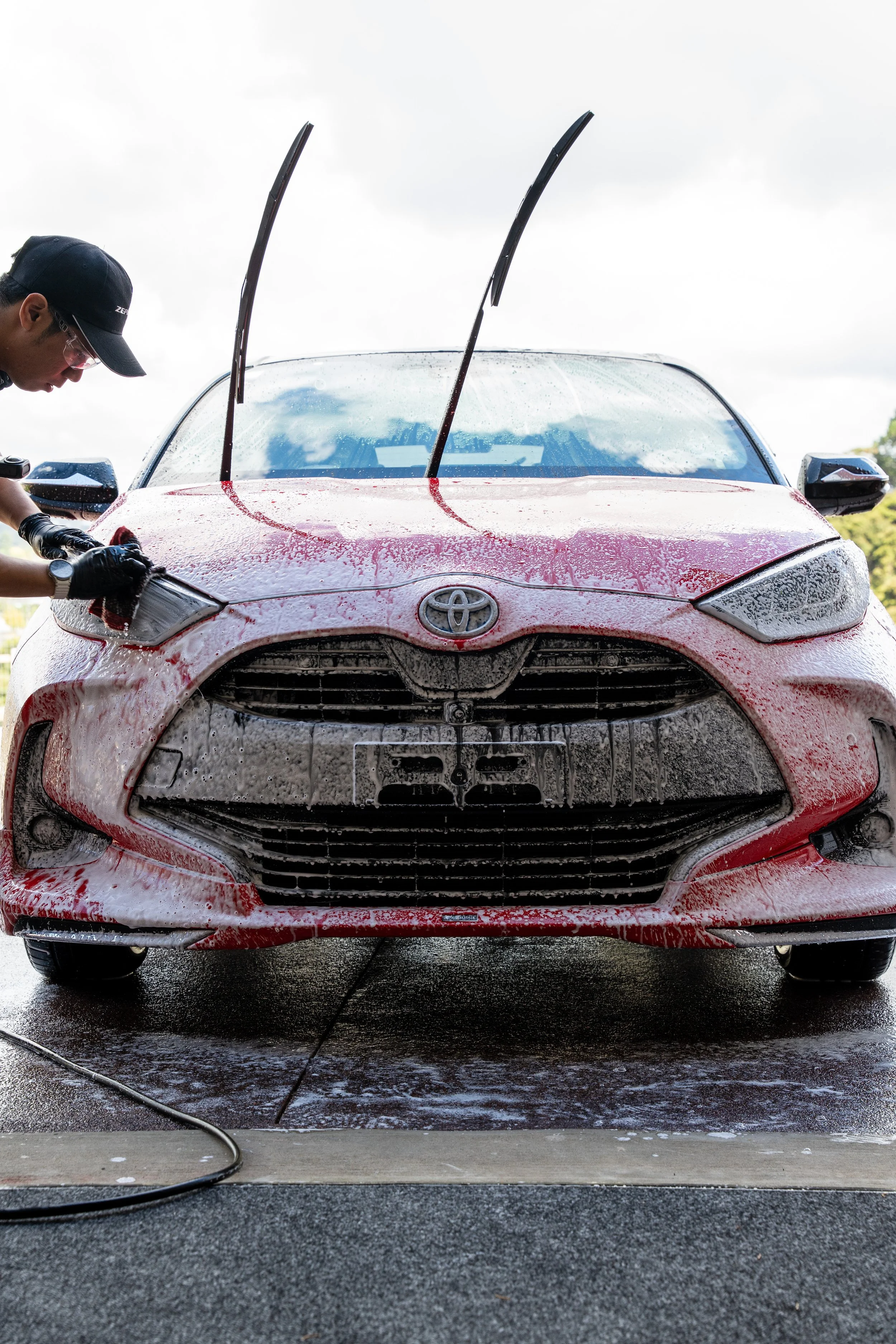 A person washing a red Toyota car with soap at a car wash station.
