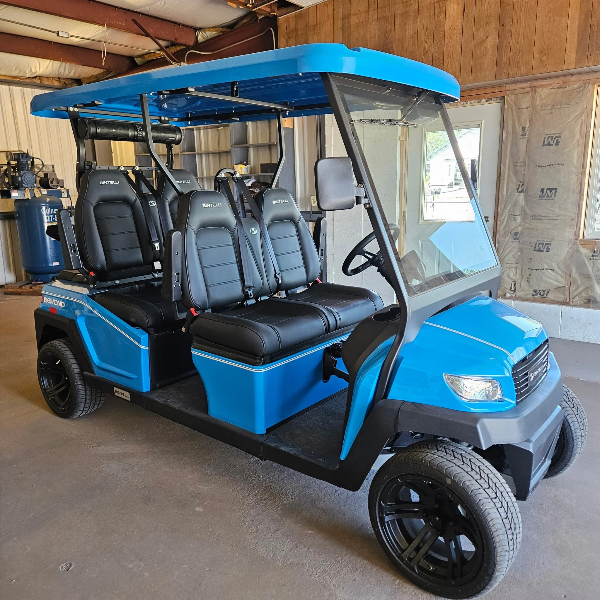 Blue golf cart with black seats and black tires parked inside a building under construction.
