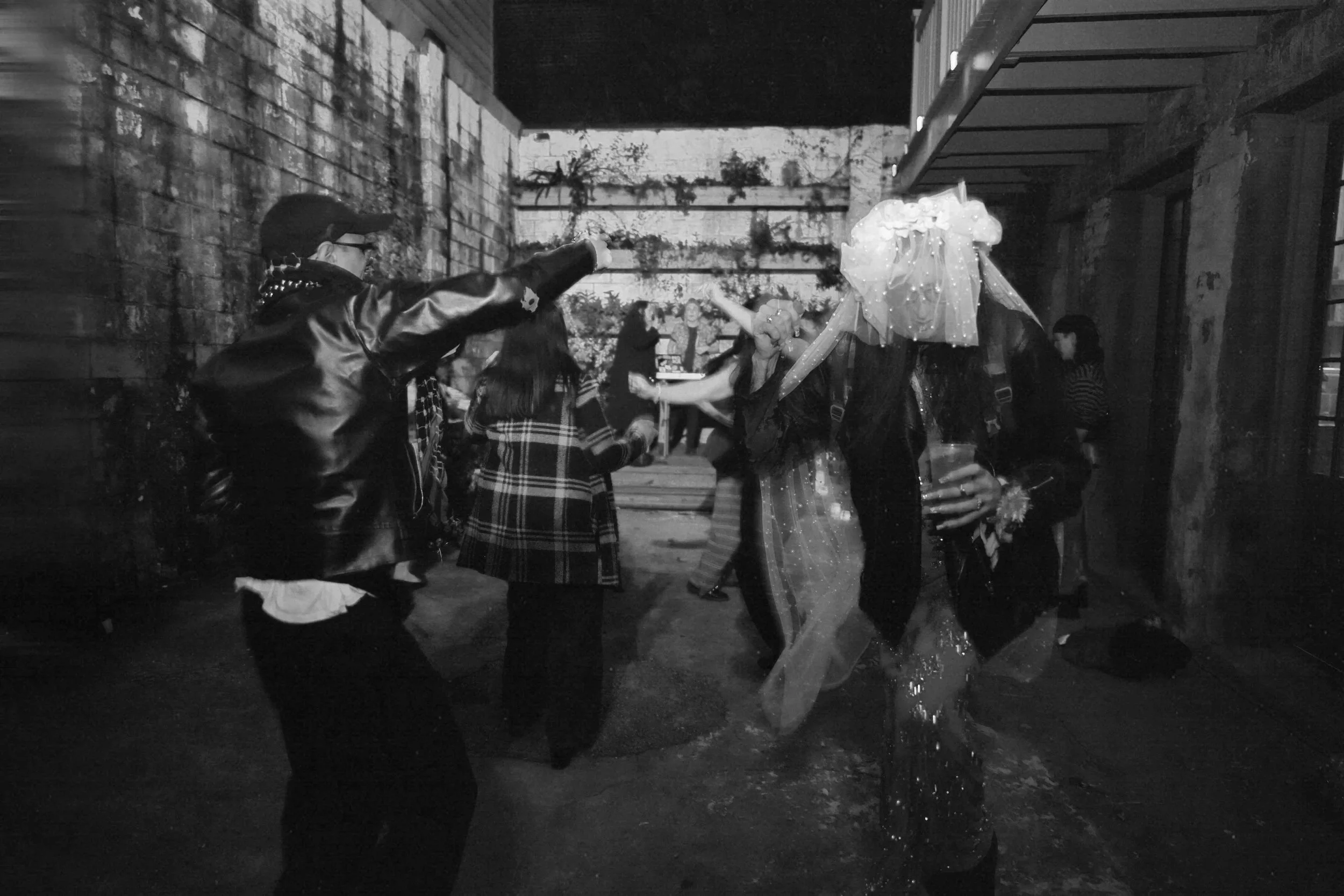 People dancing and celebrating outdoors at night, with some wearing costumes and festive attire.