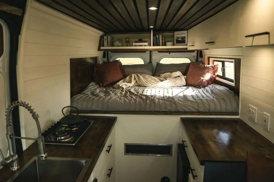 A full build in a Ram Promaster. Pop out walls to create more space in the bed area. A book shelf above the sleeping area. Propane stove a large sink area. A step was placed above the heater to allow easy access into the bed. 