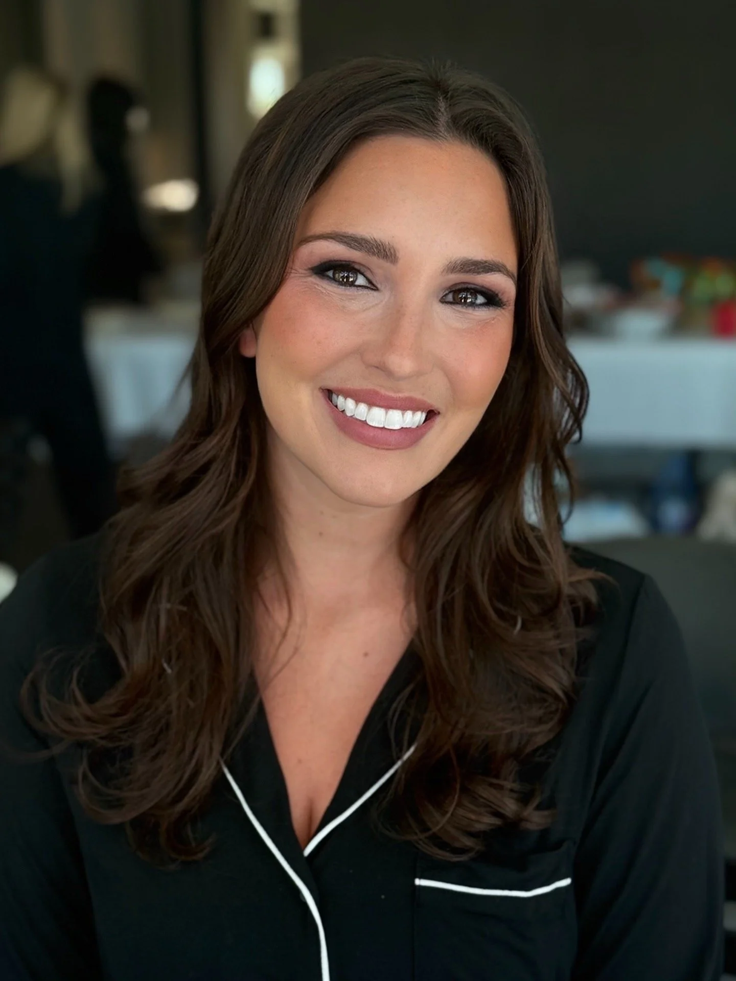 A smiling woman with long brown hair wearing white earphones and a black top with white piping.