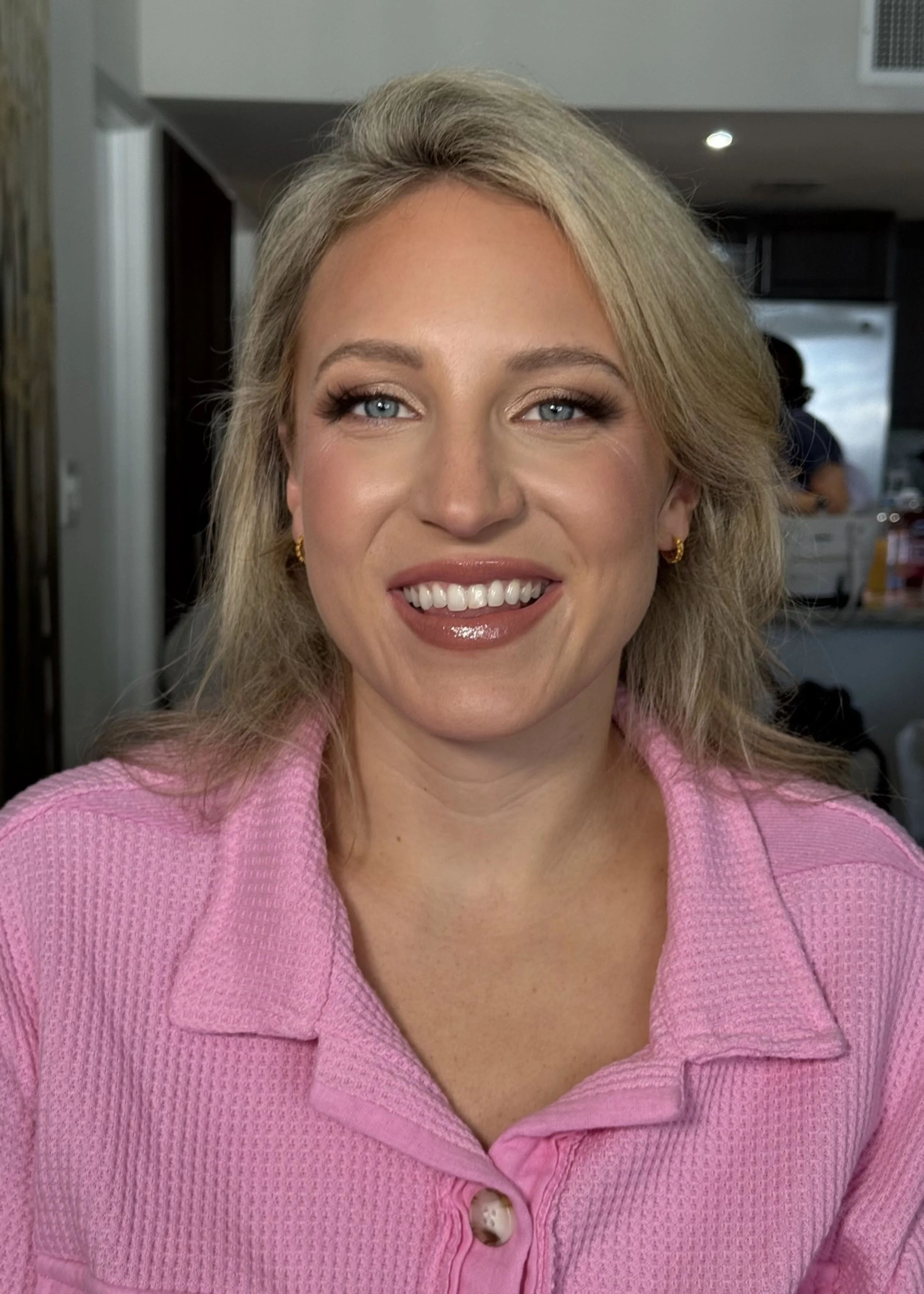 A woman with blonde hair, wearing a pink textured blazer, smiling in an indoor setting.