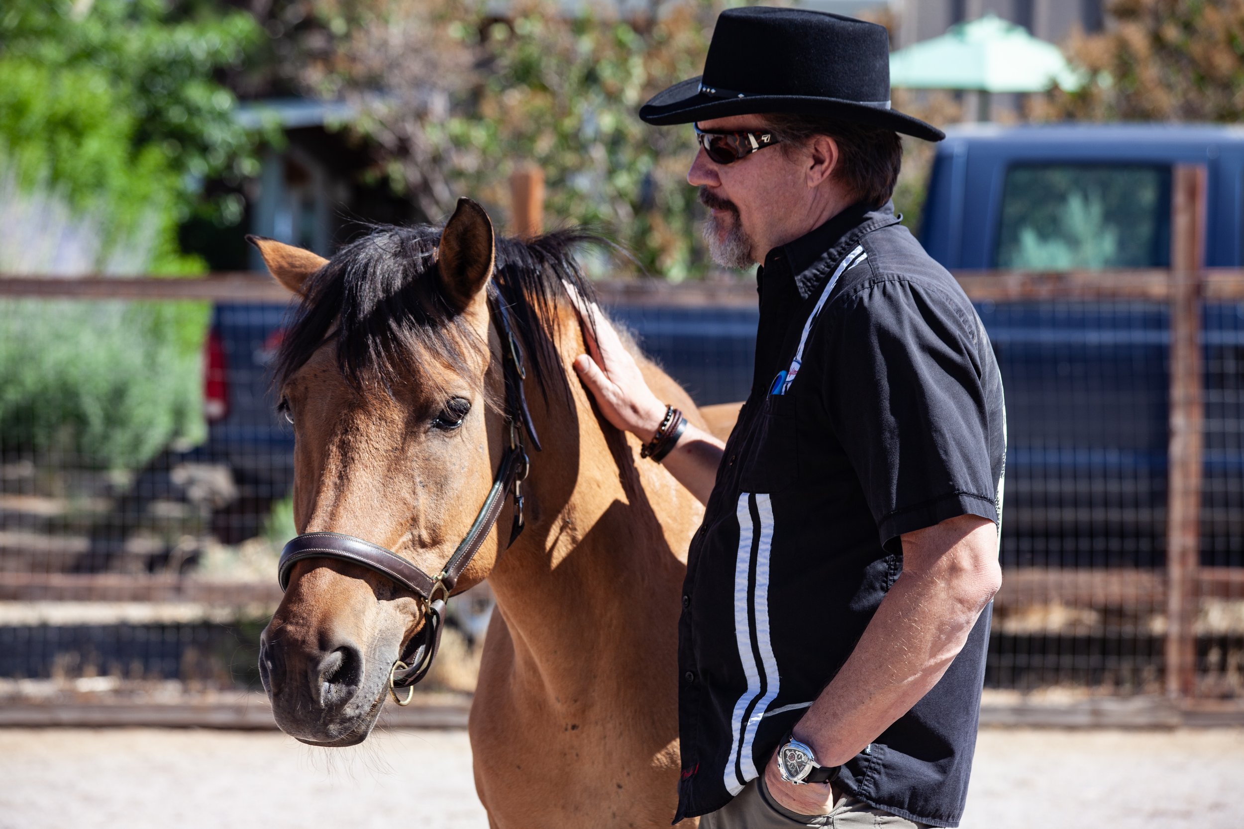 Man wearing black hat standing next to a buckskin horse with his hand on it's neck