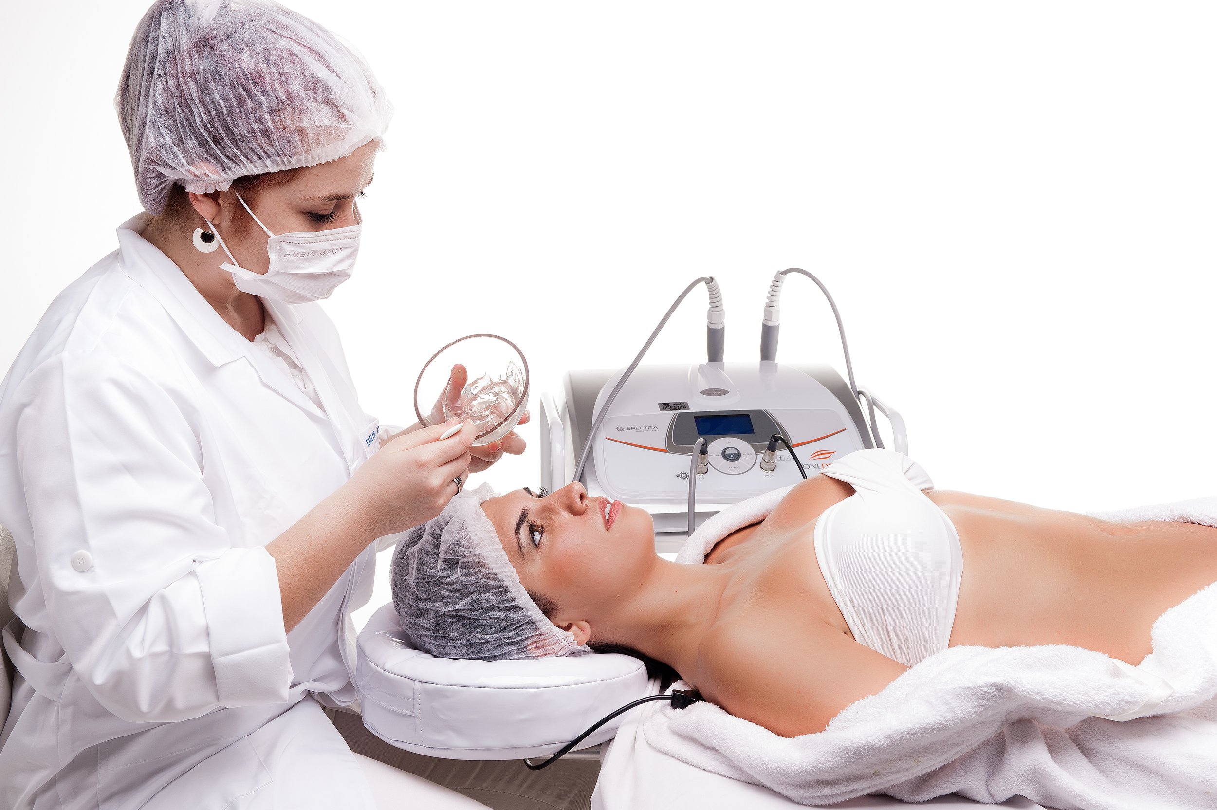 Aesthetician applying a gel to a woman receiving a beauty treatment with a machine.
