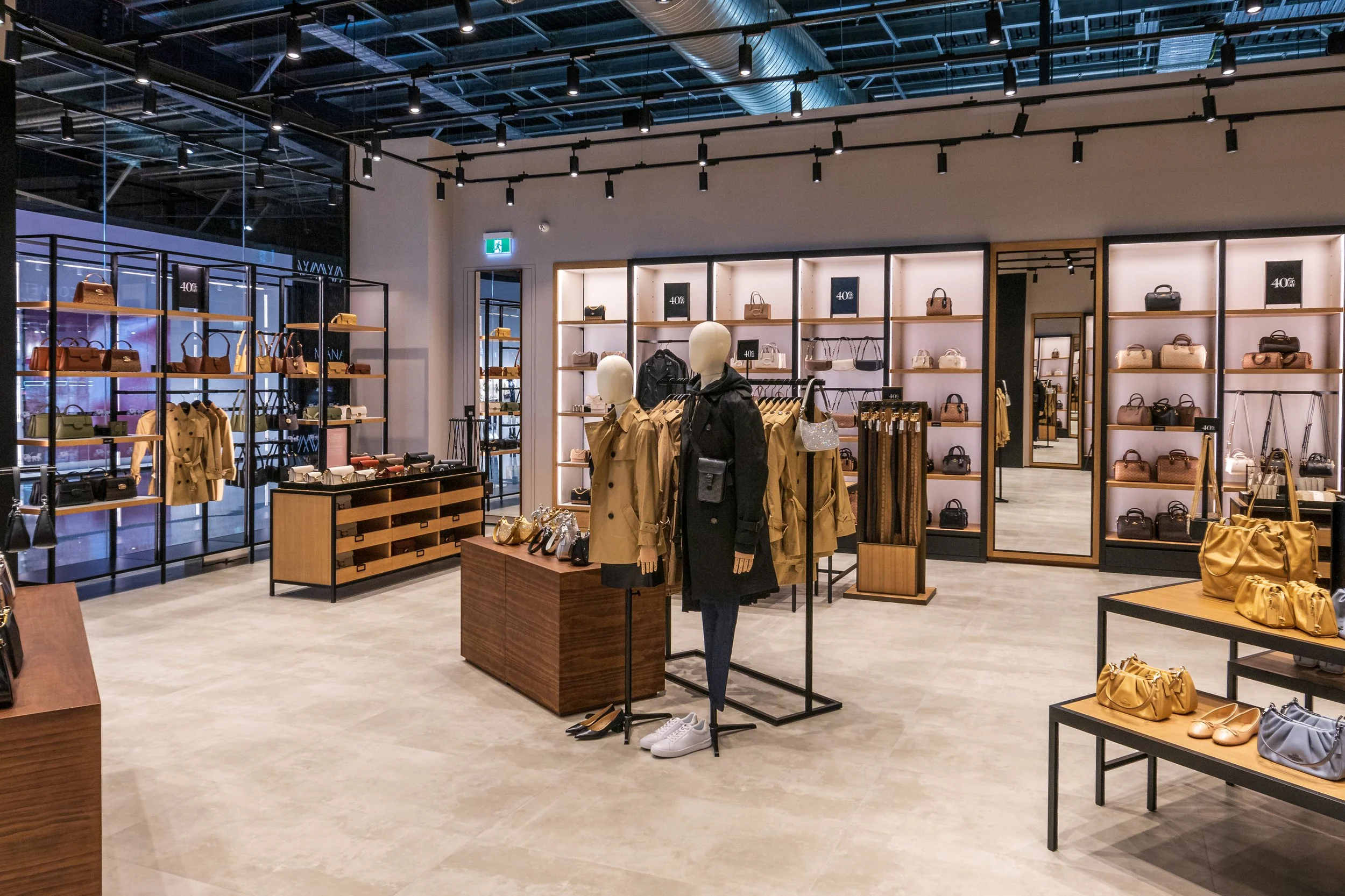 Fashion retail store interior featuring mannequins in coats, shelves displaying handbags and shoes, and modern lighting.
